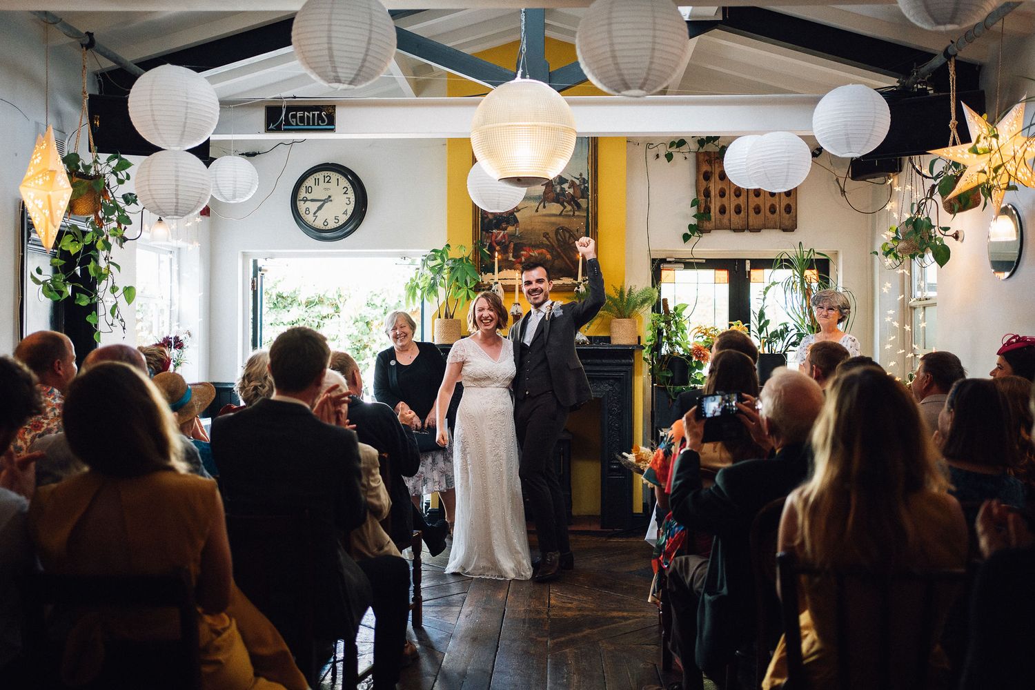A wedding celebration in a cozy restaurant venue decorated with white lanterns and warm lighting as guests look on.