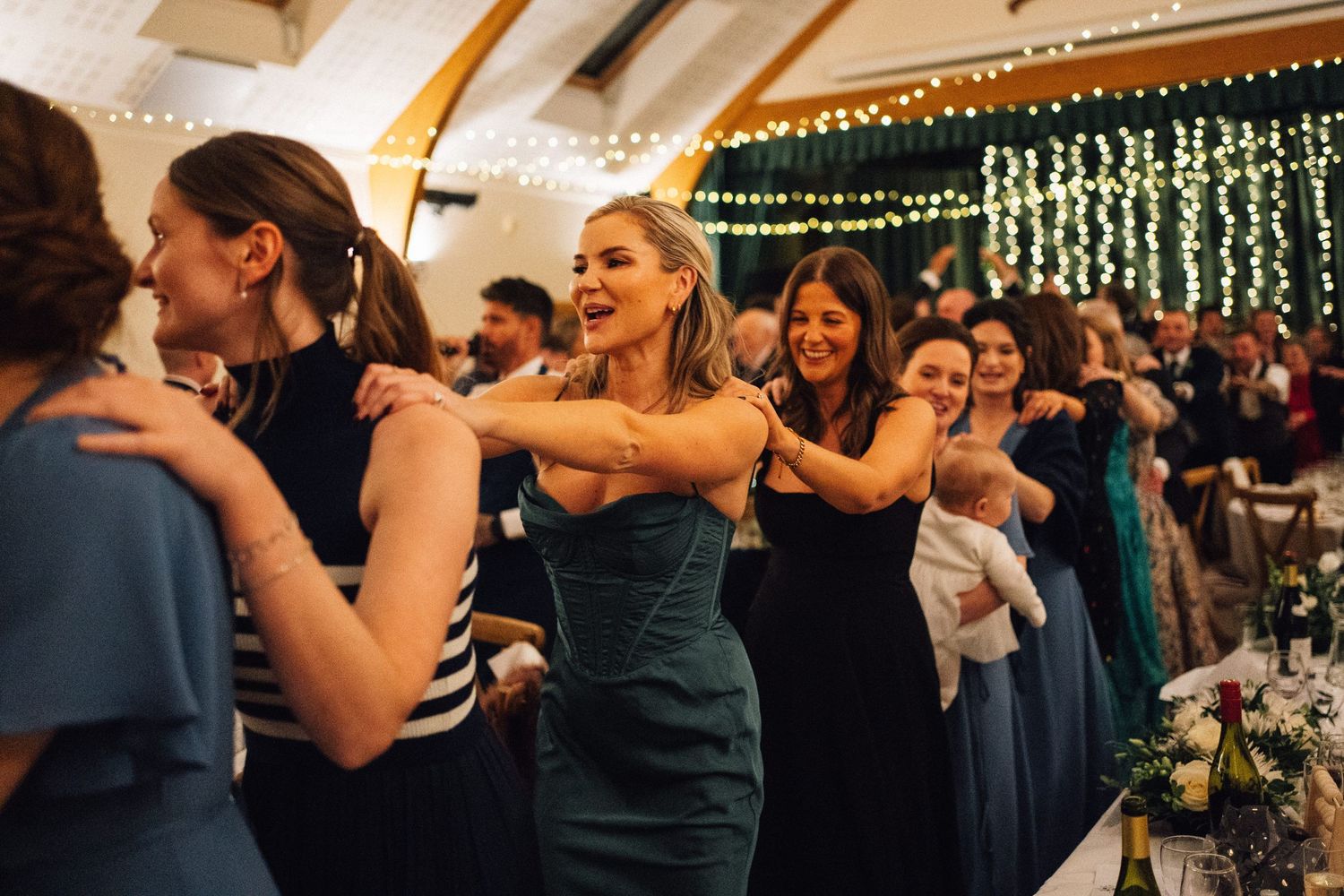 Wedding guests dance together at an evening reception with string lights decorating the venue.