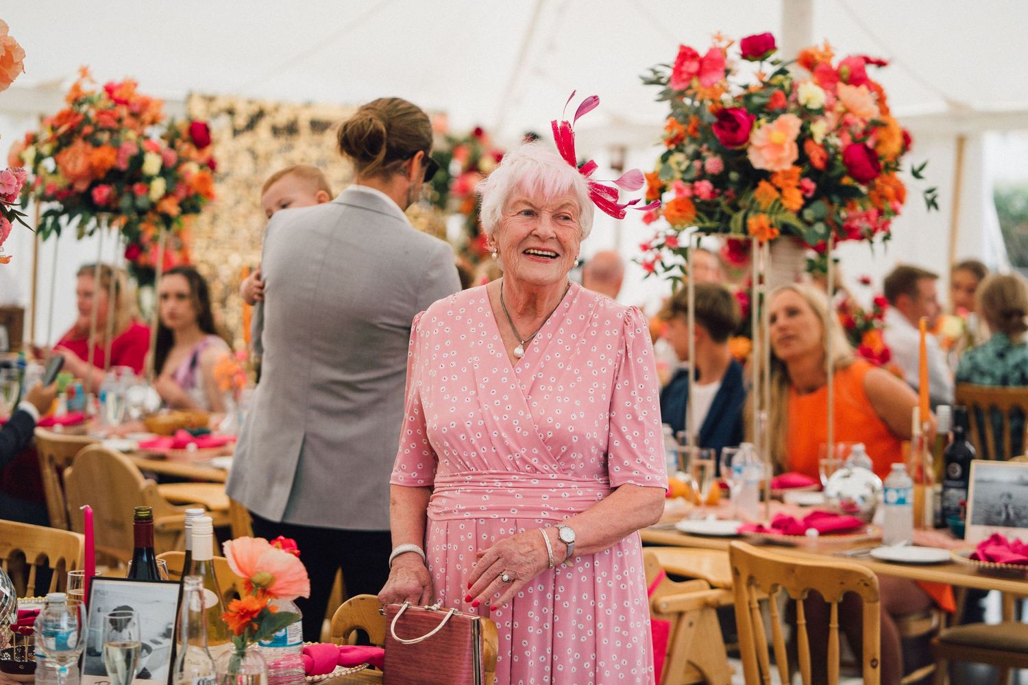 Colorful floral arrangements and table settings decorate a bright indoor event space with guests seated at round tables.