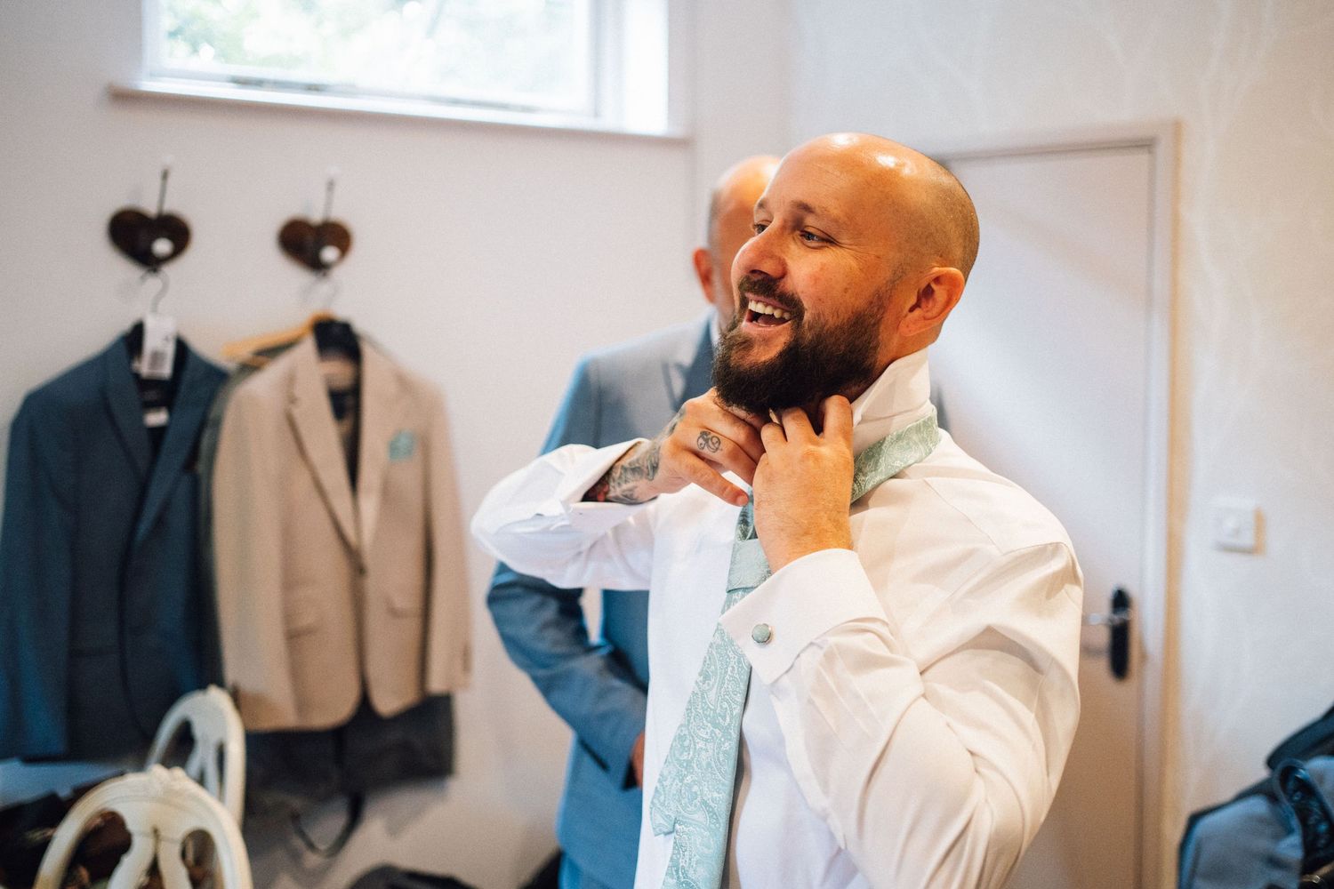 Wedding preparation scene showing formal attire and suits hanging in a bright white dressing room.