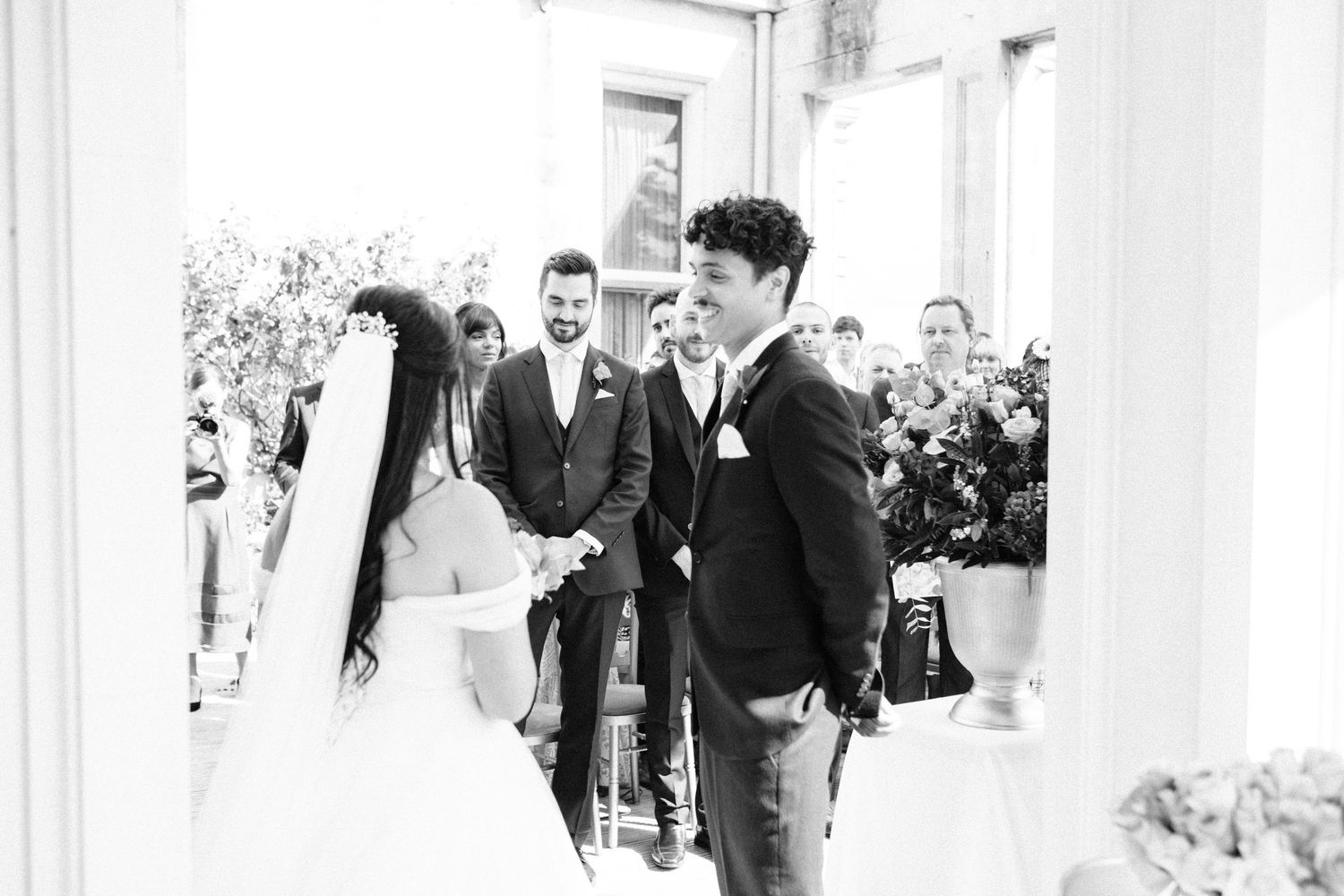 A black and white photo capturing a wedding ceremony moment in a bright, columned space.