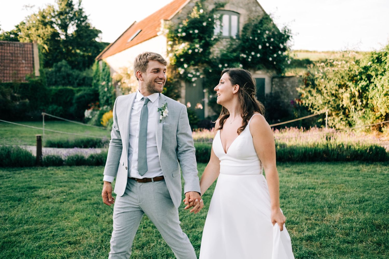 Couple shares joyful moments on a sunny lawn during an elegant outdoor wedding celebration.