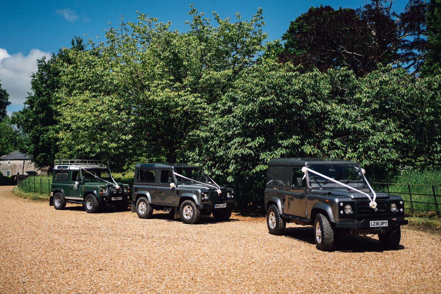 Three black Land Rover Defenders lined up as wedding vehicles on a gravel driveway.