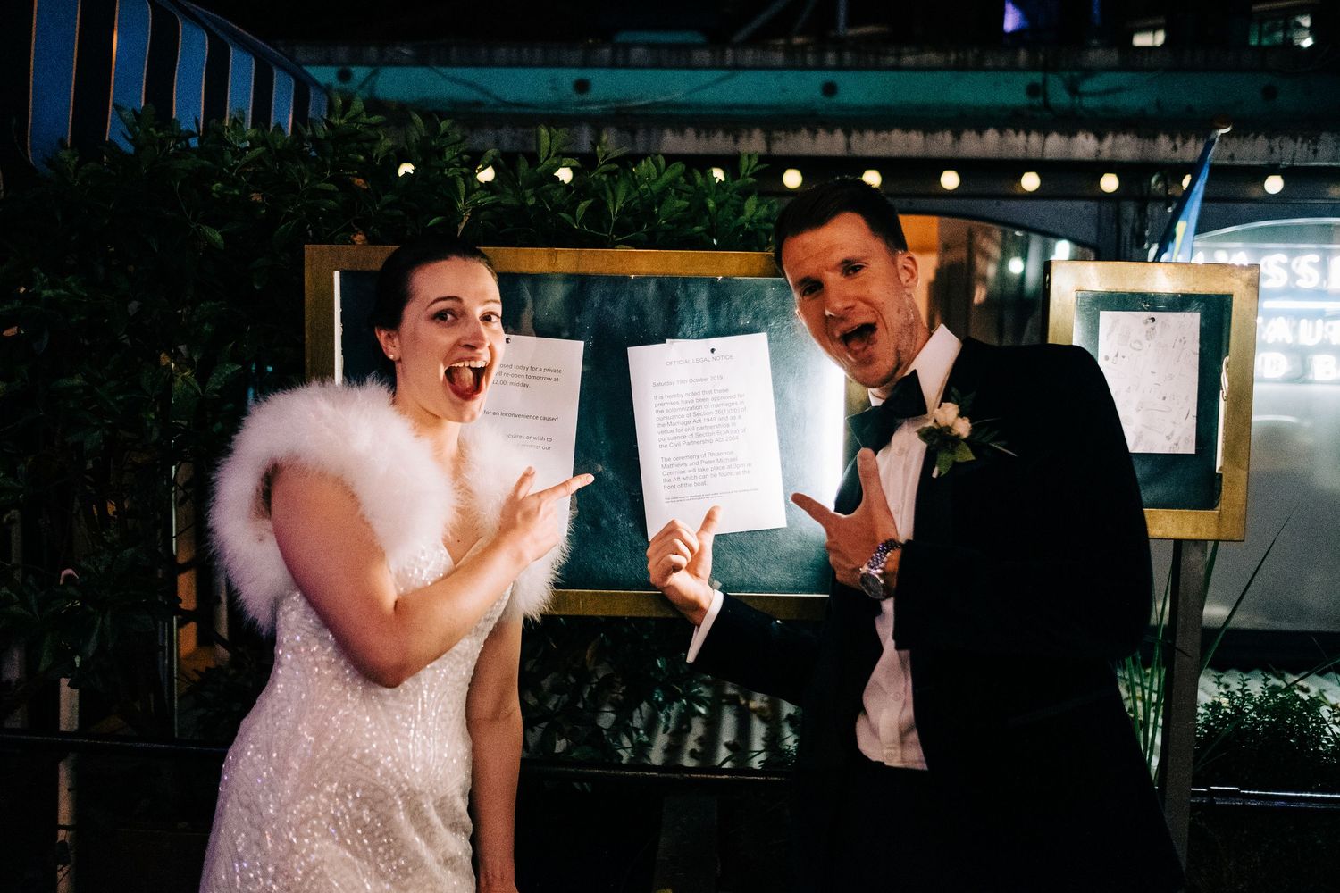 A couple celebrates joyfully while holding up documents at their wedding reception.