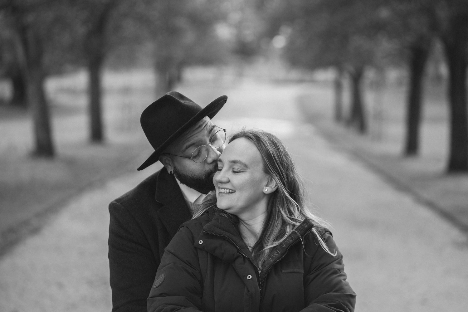 Black and white portrait of a couple sharing an intimate moment in a park setting.