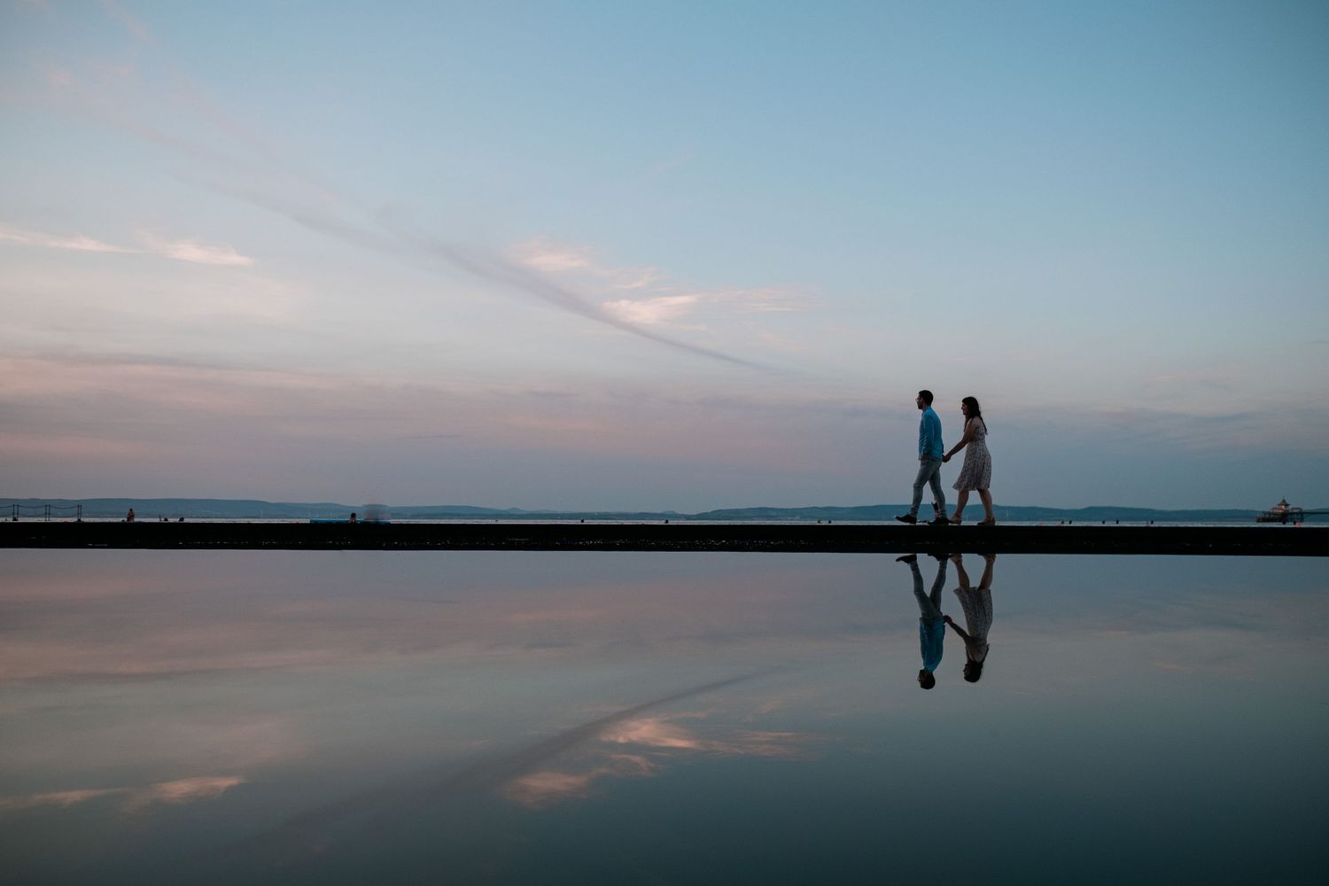 Two people walking on reflective surface during sunset with perfect mirror reflection.