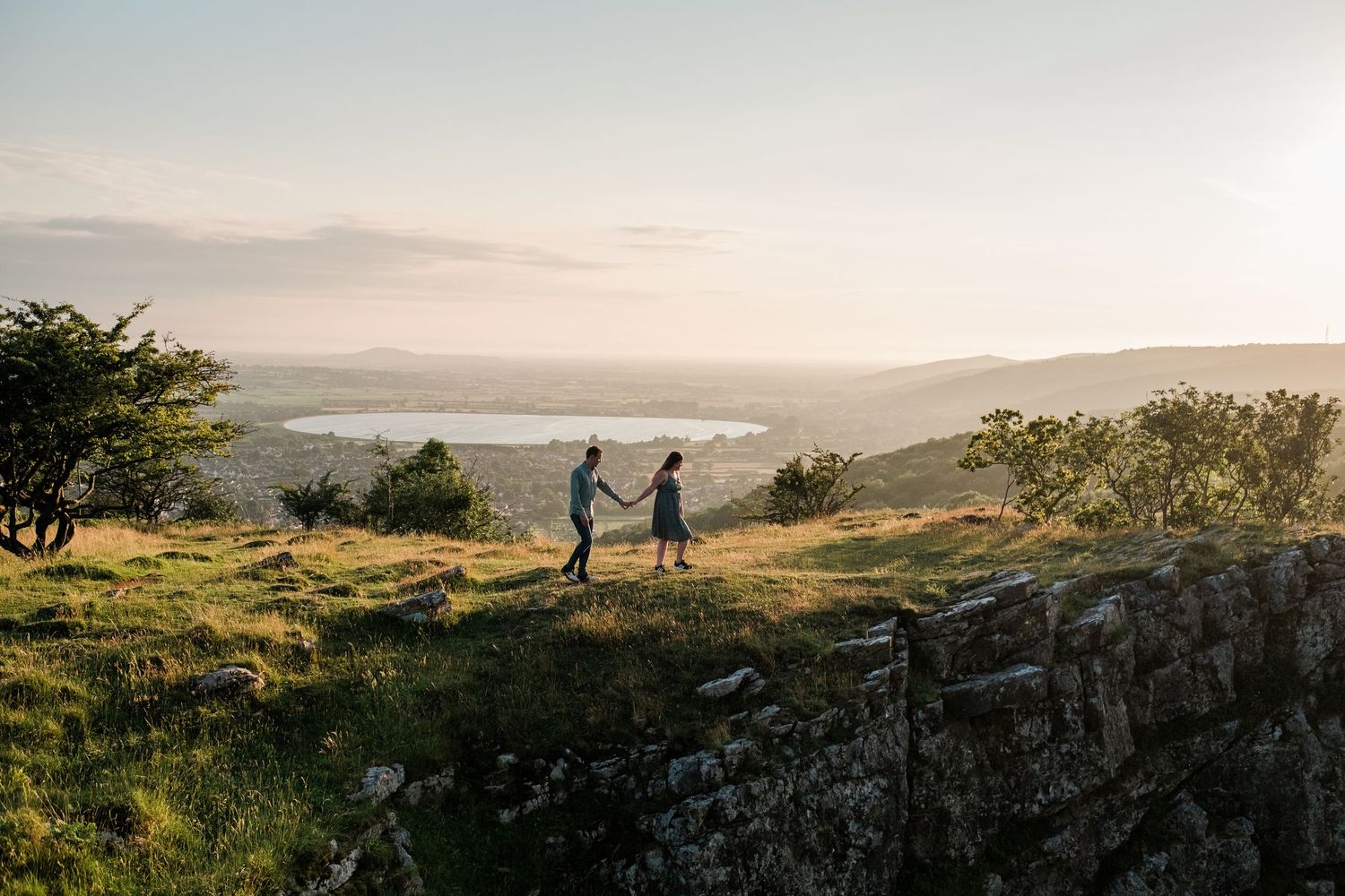 Panoramic view of rolling hills and countryside at sunset with figures in the distance.
