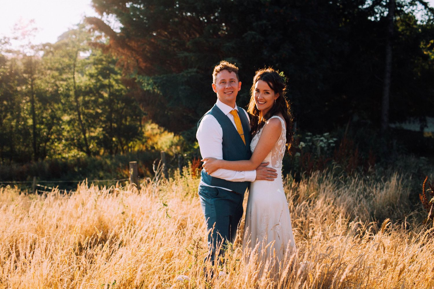 Intimate wedding moment captured in golden sunset light among tall grass.