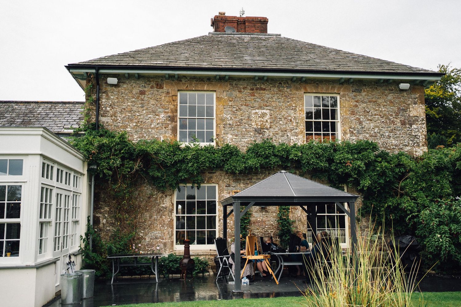 Stone country house with ivy-covered walls and outdoor seating area under a dark umbrella.