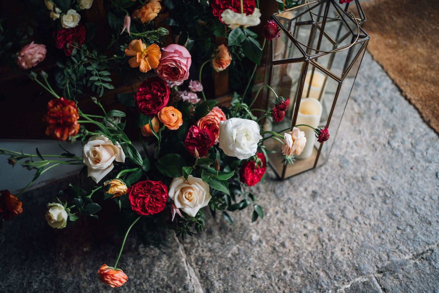 Elegant floral arrangements with dark red and blush roses displayed against a rustic stone surface with lantern decor.