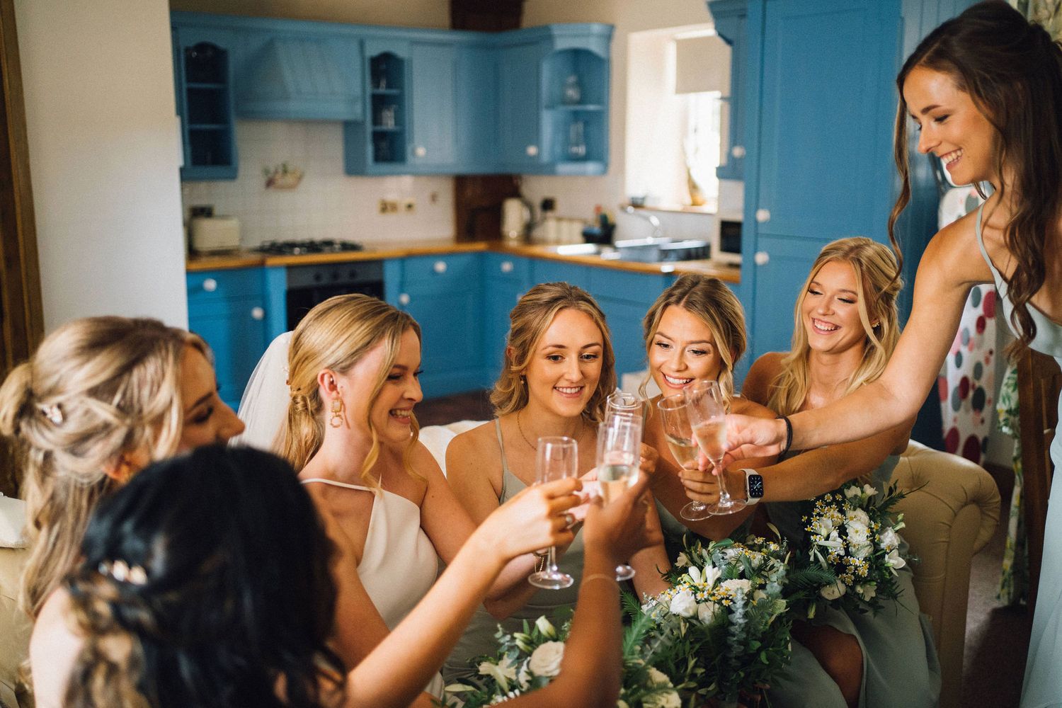A group of people raise champagne glasses in celebration during a wedding reception in a bright indoor venue.