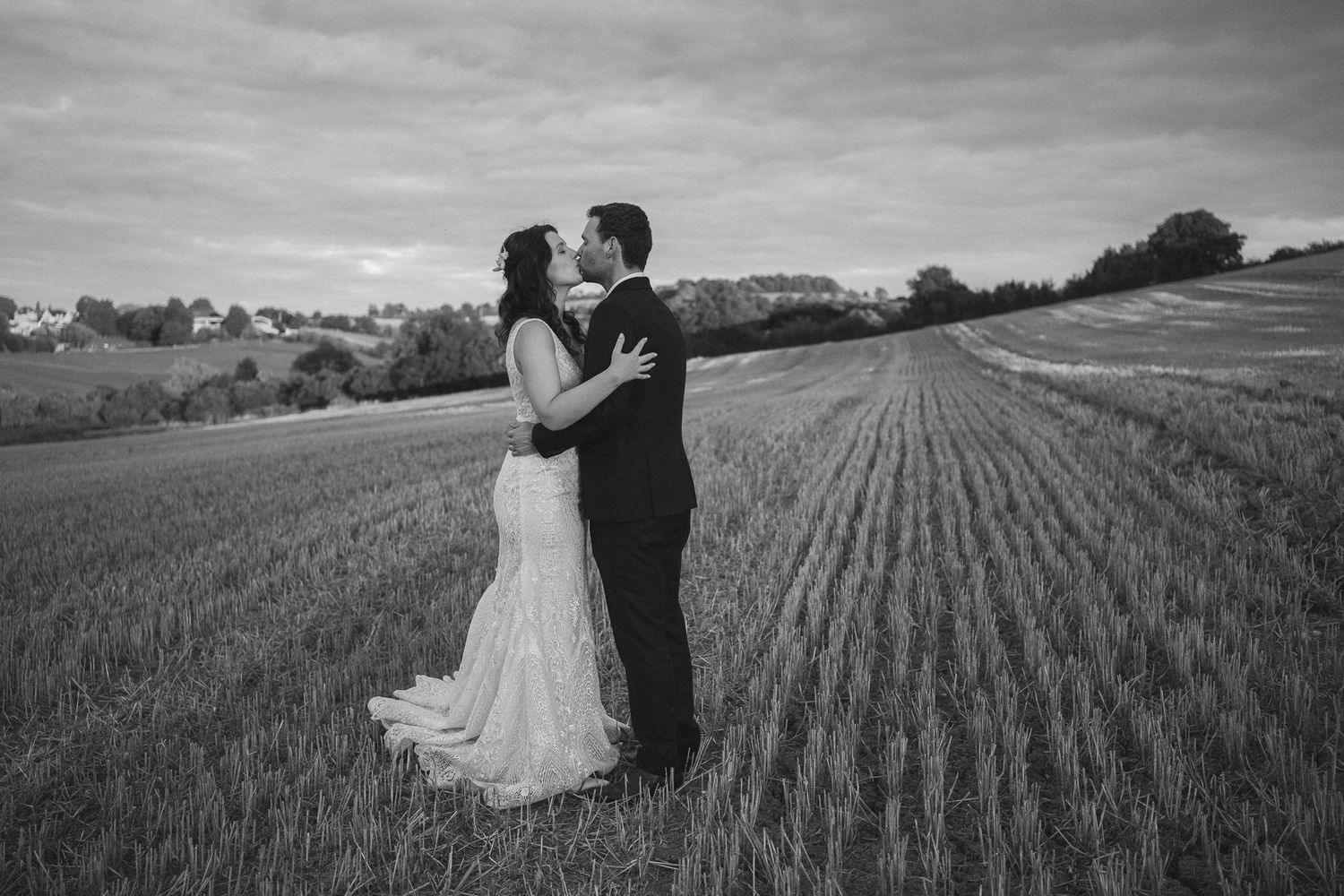 Black and white photo of a bride and groom kissing in a field on their wedding day.