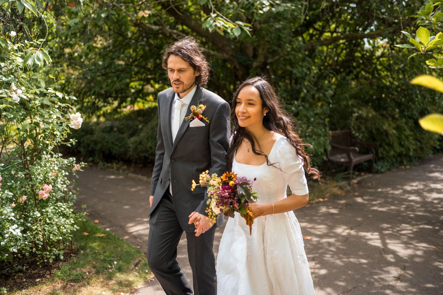 Bride and groom walking hand in hand through a lush garden on their wedding day.