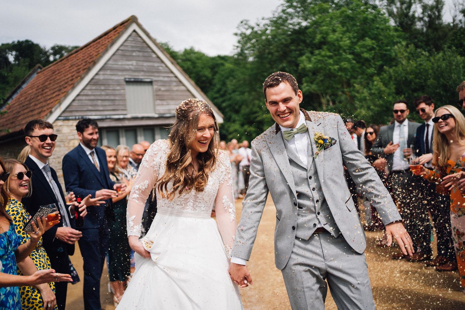 Wedding guests celebrate outdoors near a rustic barn as confetti fills the air.