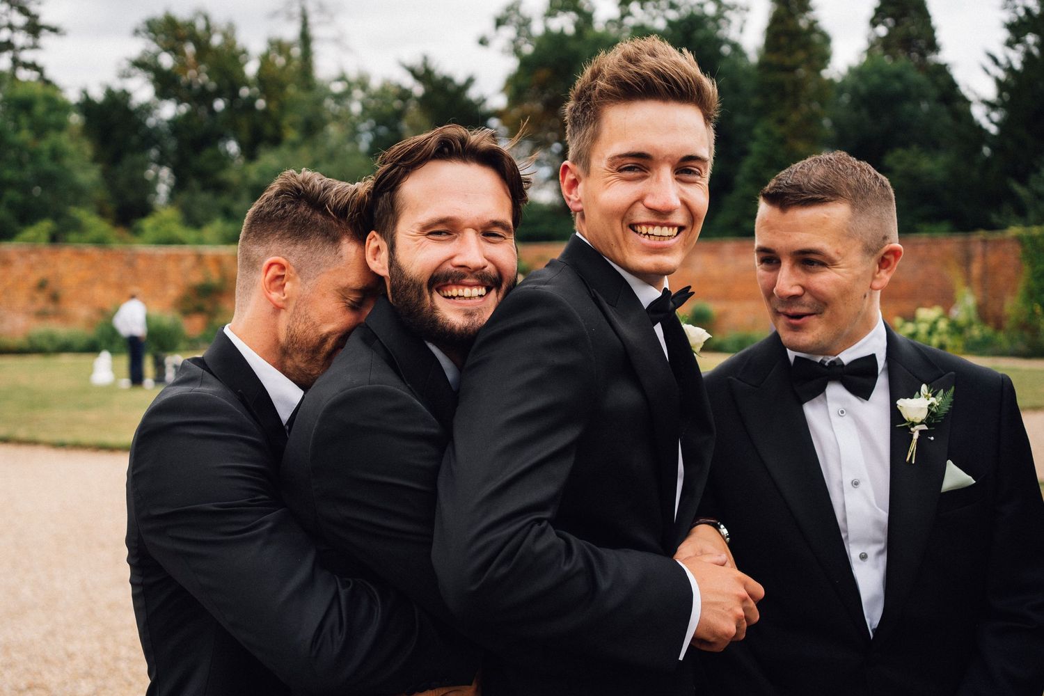 Groomsmen in black tuxedos share a candid laughing moment together during a wedding photoshoot outdoors.