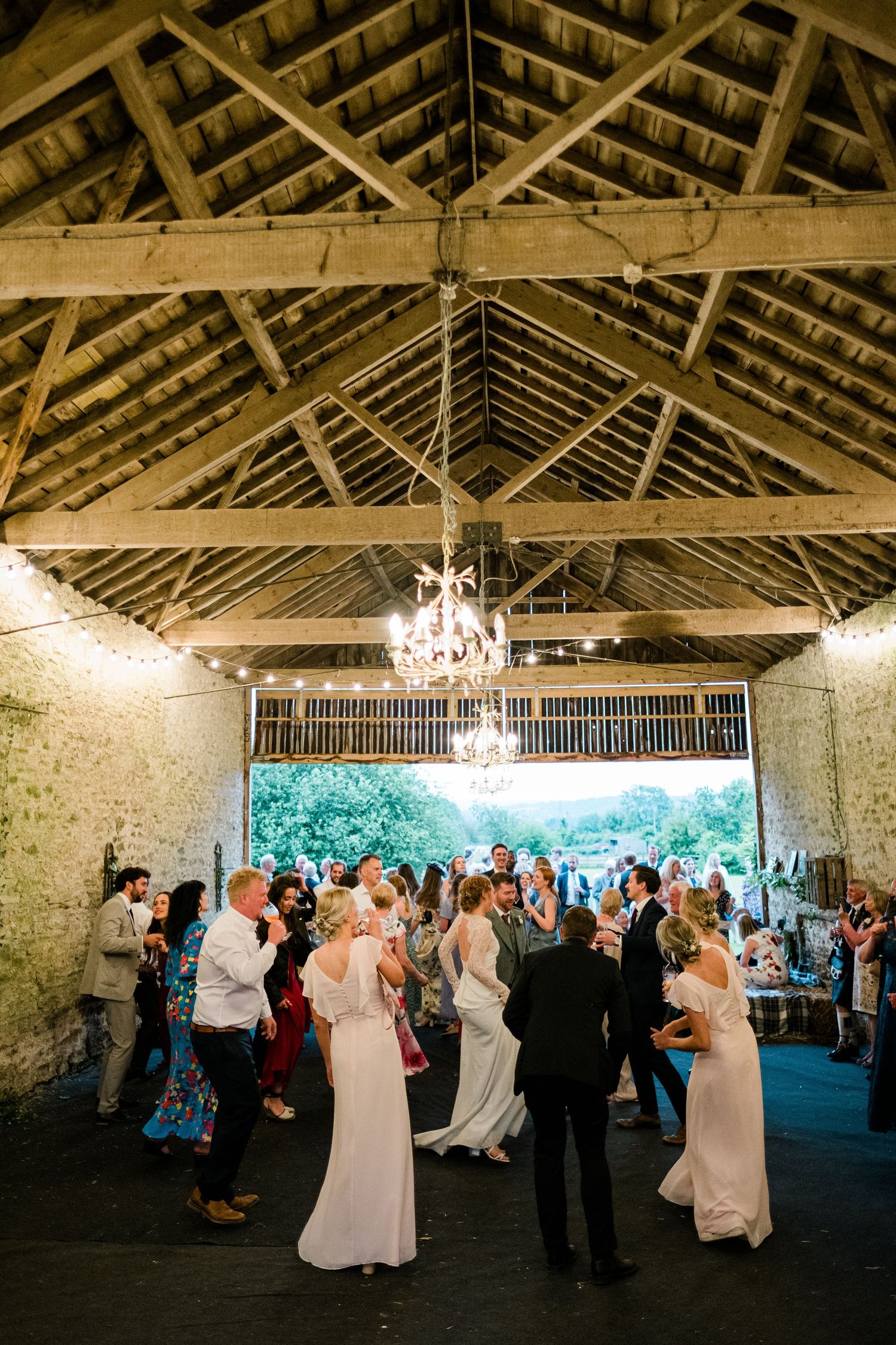 Wedding reception dance floor in a rustic barn with exposed beams and chandeliers.