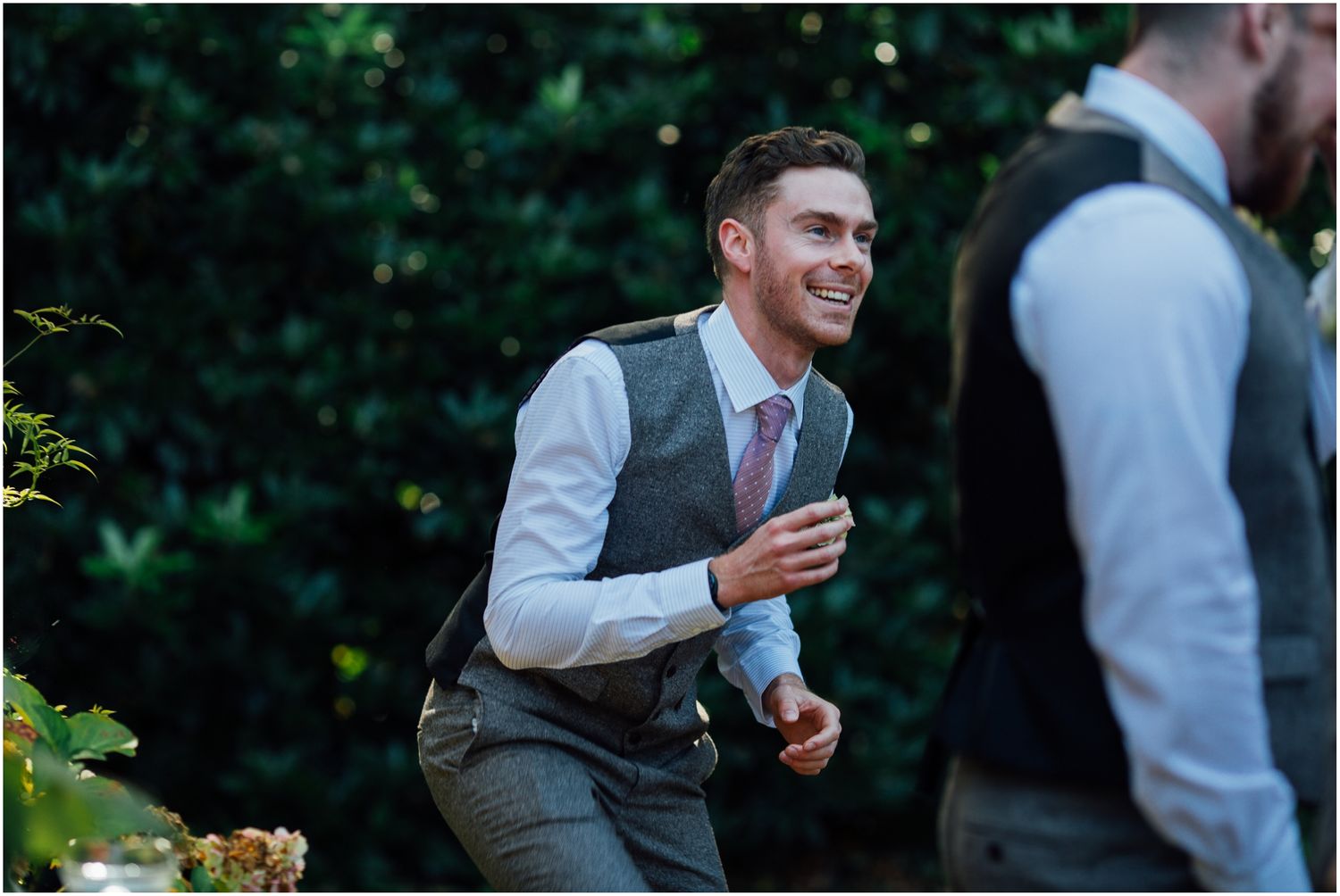 Wedding guest in grey vest laughing during outdoor reception.
