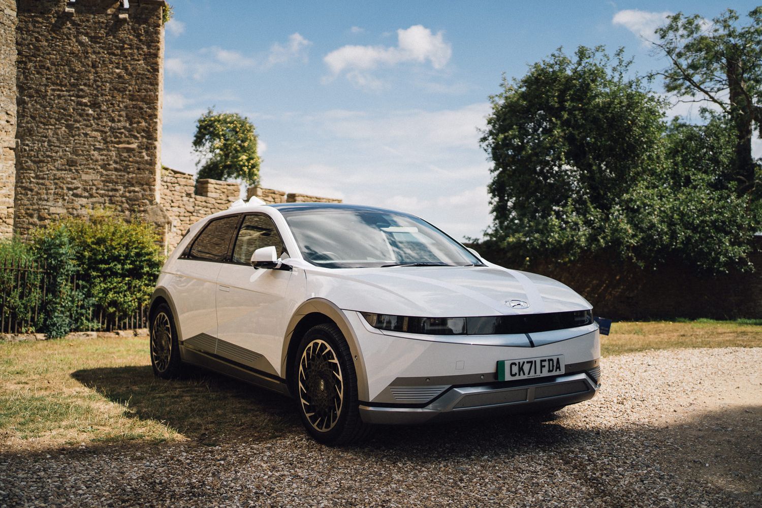A white Hyundai Ioniq 5 electric car parked near stone walls on a sunny day.