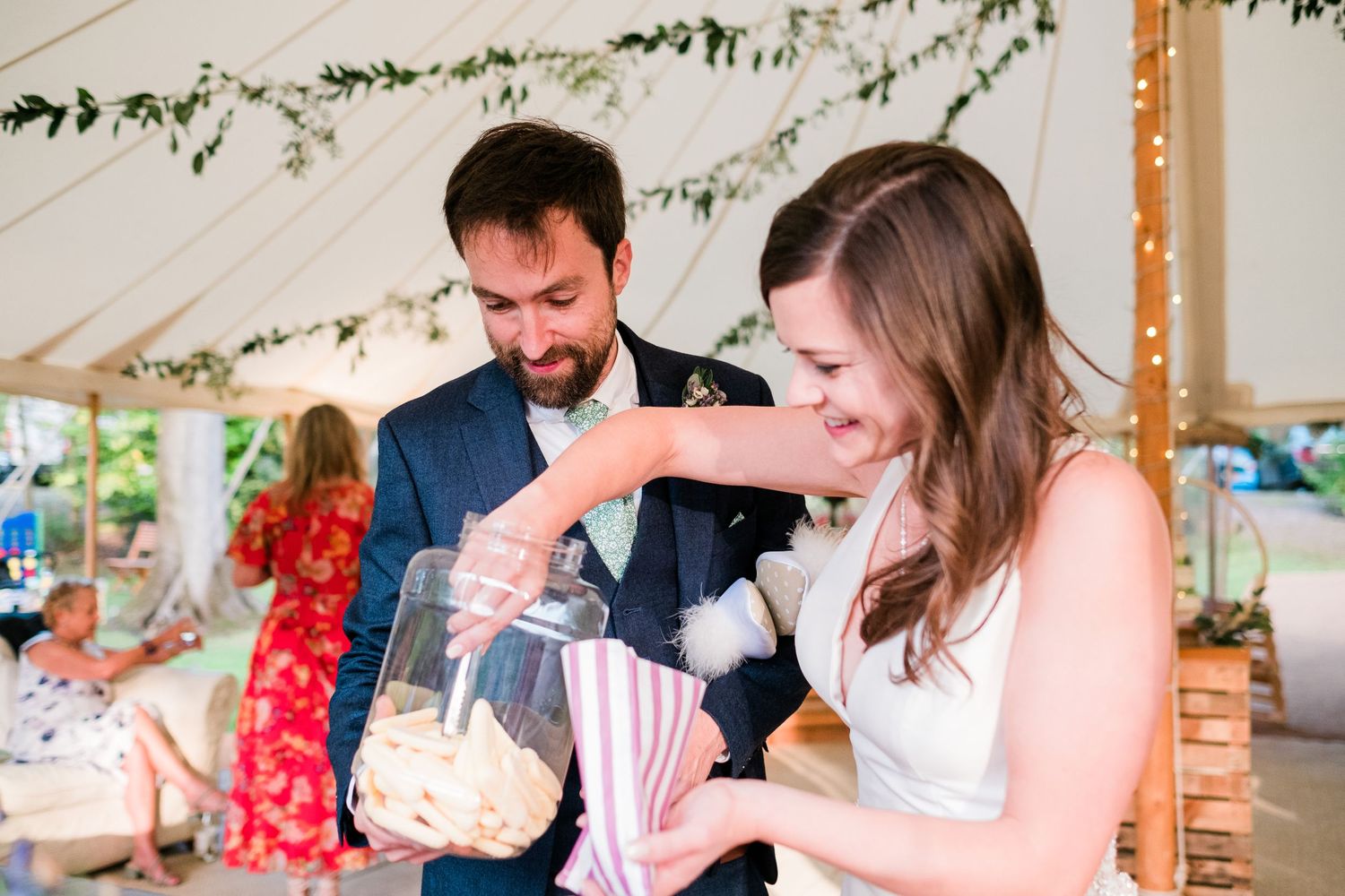 Wedding reception tent decorated with hanging greenery garlands and string lights creates an enchanting atmosphere.