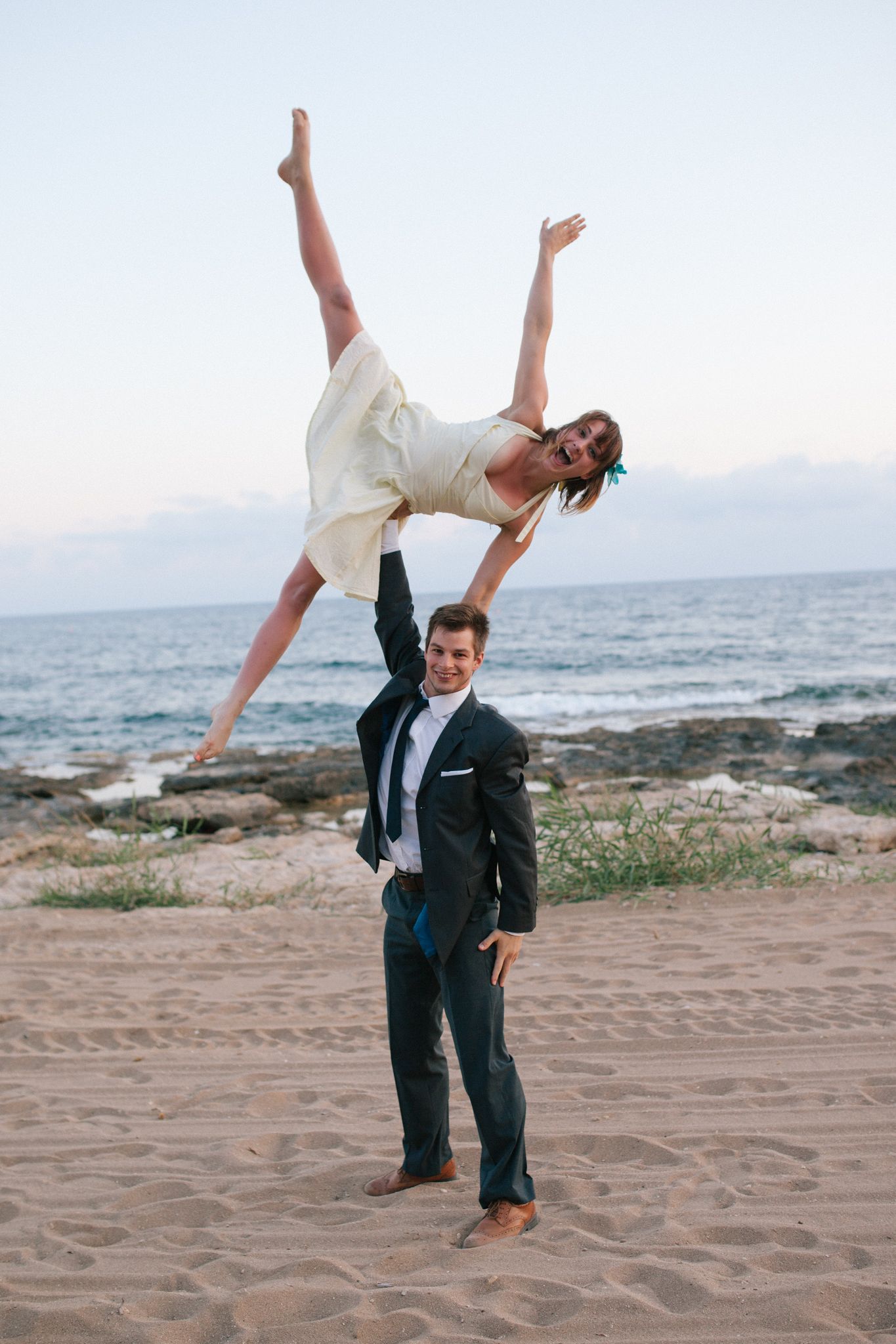 A couple performs a dramatic dance lift pose on a beach at sunset.