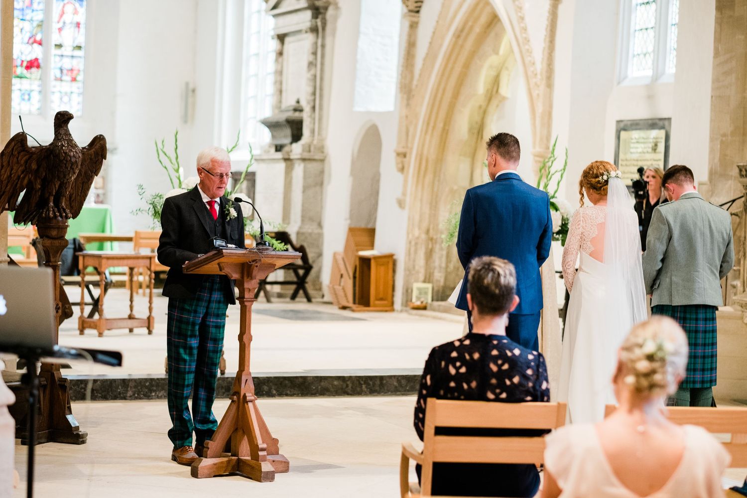 Wedding ceremony taking place in bright, airy cathedral with stone archways.