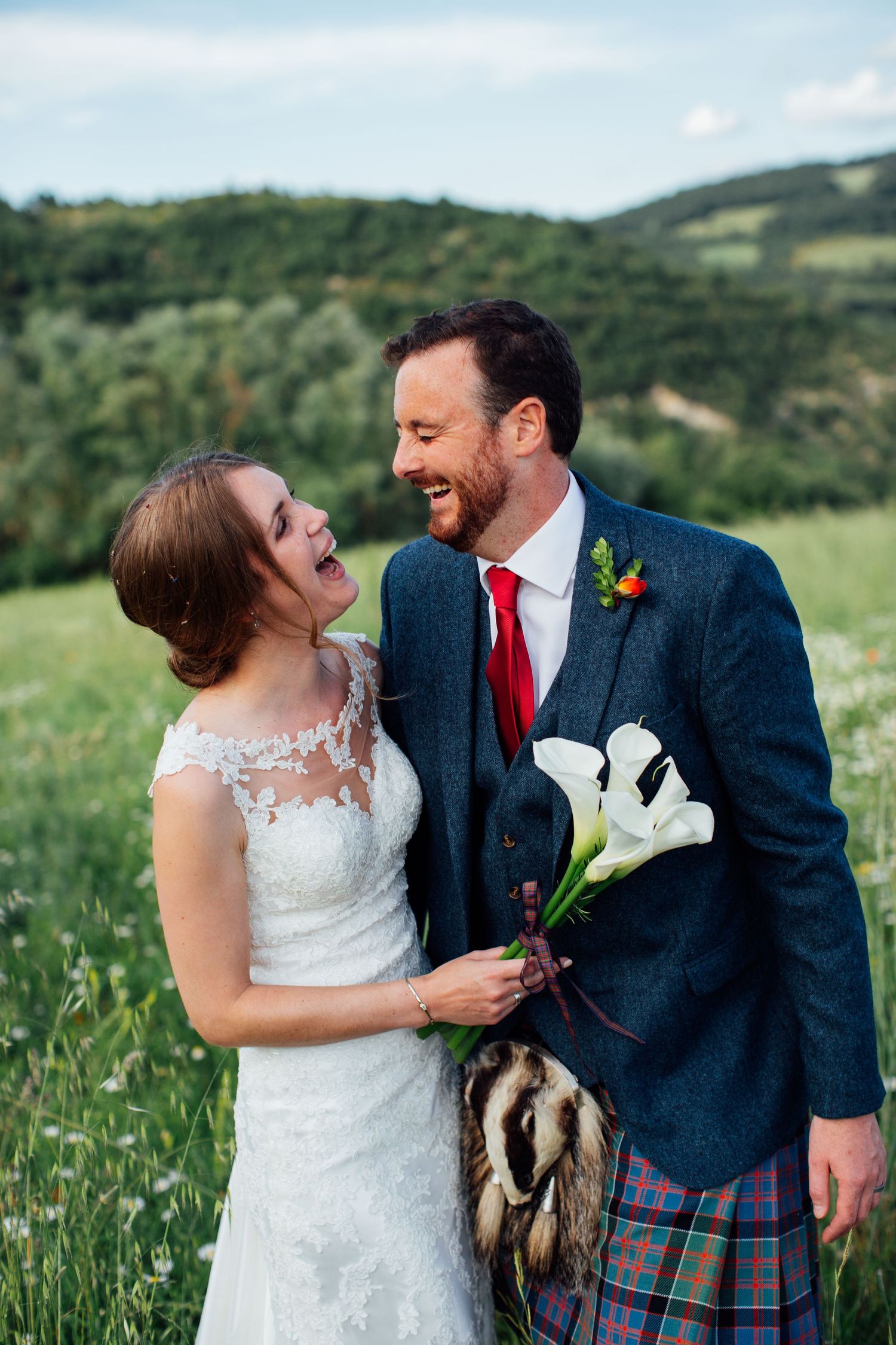A wedding couple poses in a meadow with the groom wearing a traditional Scottish kilt.