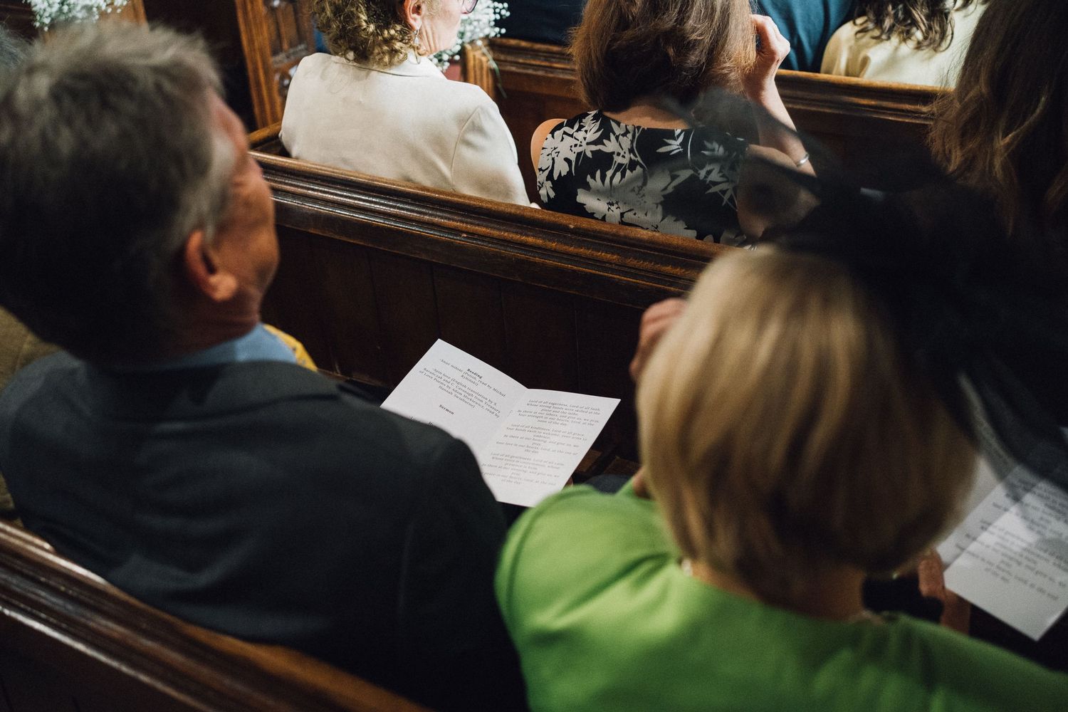 Wedding guests seated in church pews during ceremony with natural light streaming through windows.