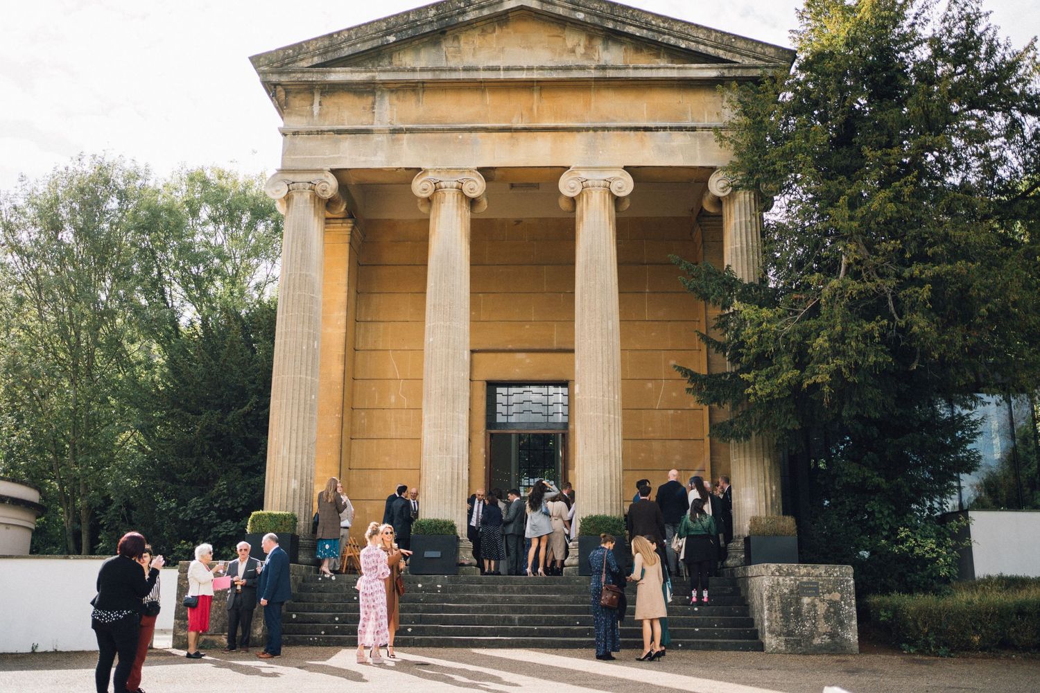 Classical stone temple building with columns stands in a lush garden setting.