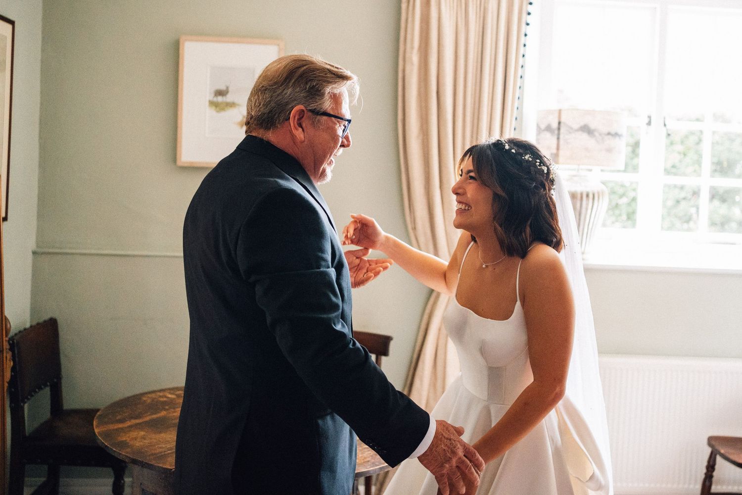 A heartwarming moment between two people in a bright room, one in a wedding dress and one in a suit.