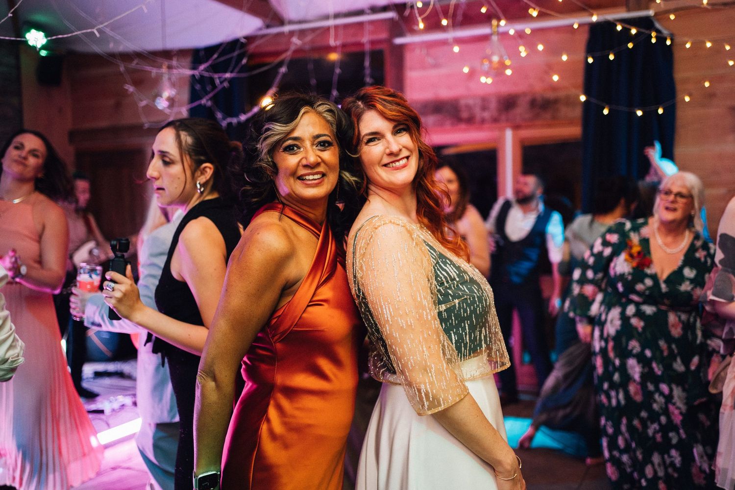 Wedding reception dance floor filled with guests under colorful lighting.