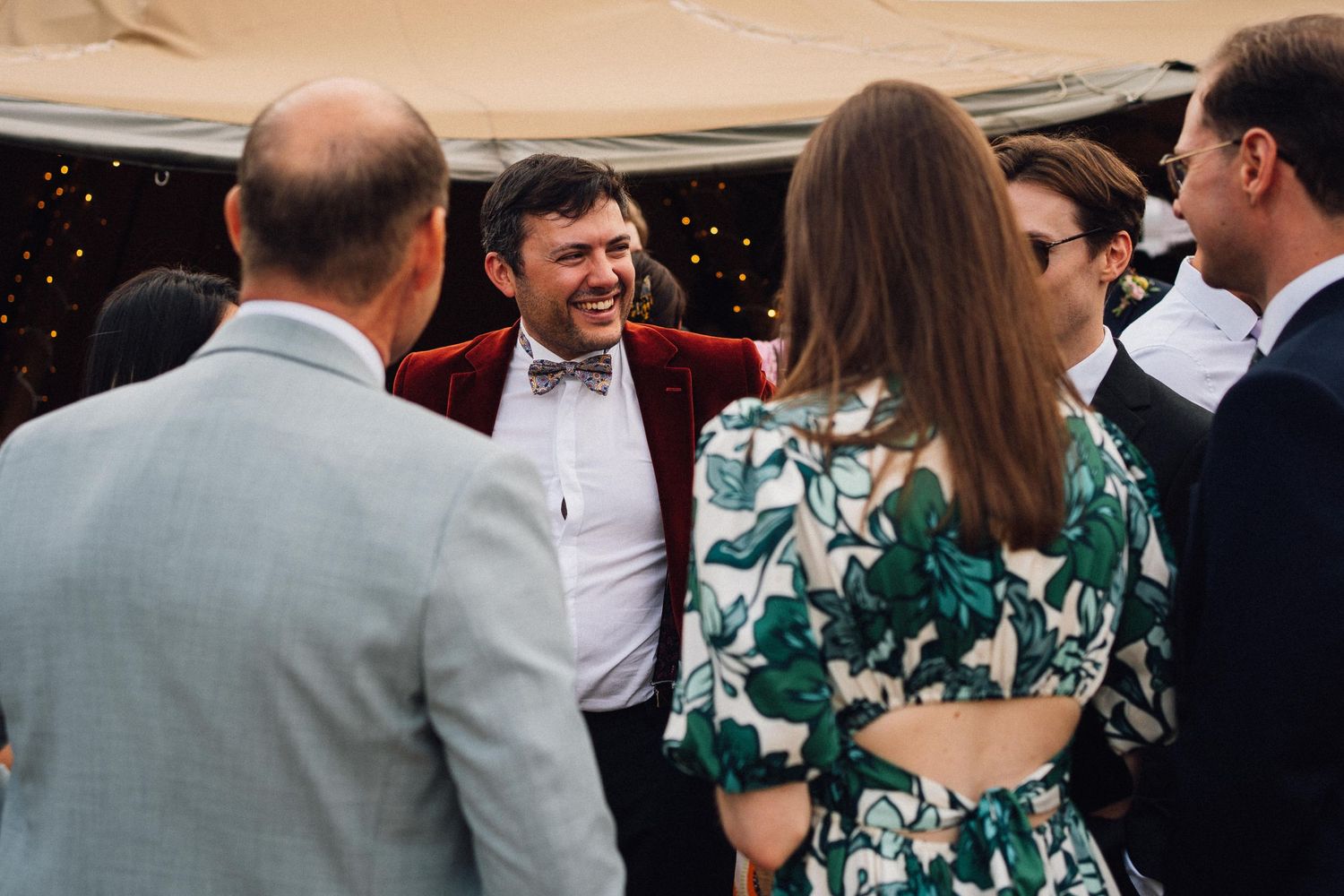 Wedding guests enjoy an elegant outdoor reception under a white tent with string lights.