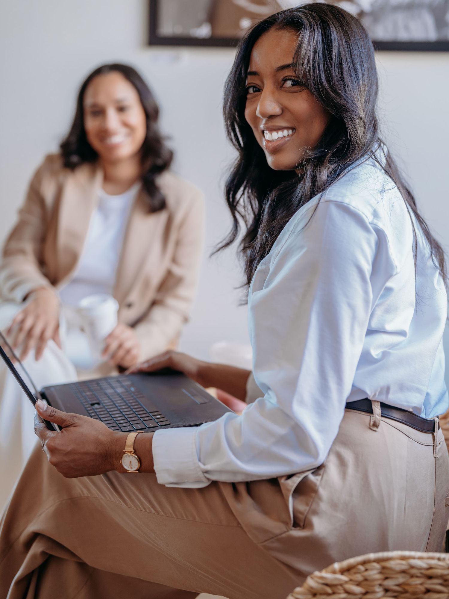 Professional colleagues collaborate in a bright office space with one using a laptop while wearing business attire.