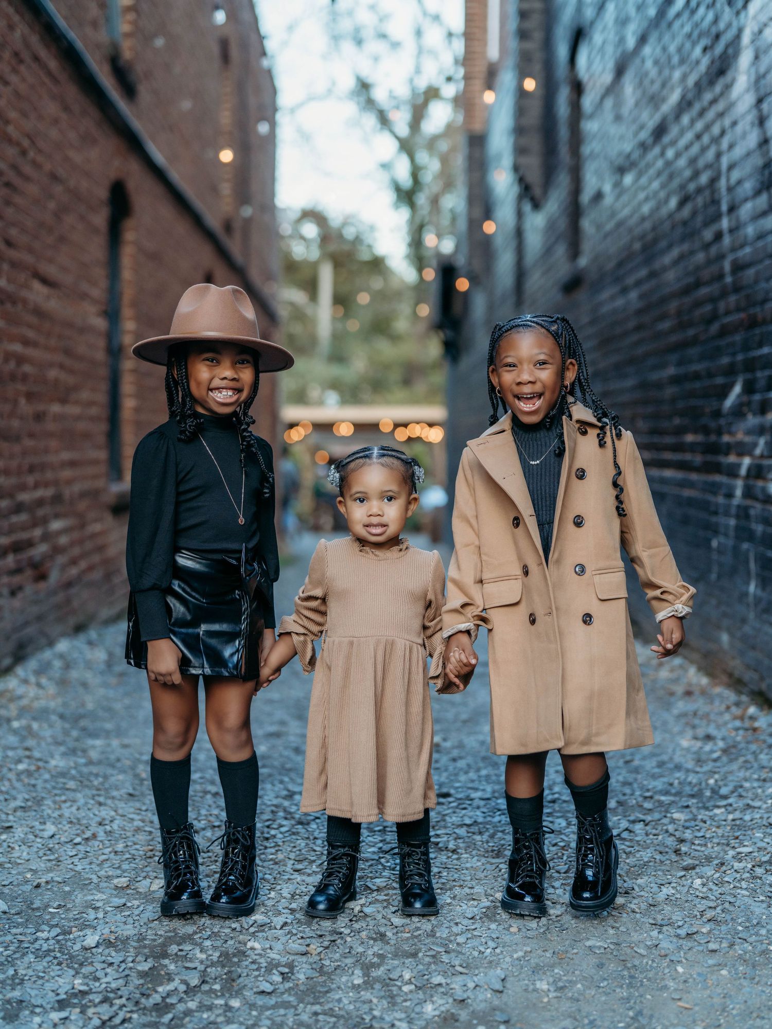 Four children in matching outfits pose together against a brick wall in an urban alley setting.