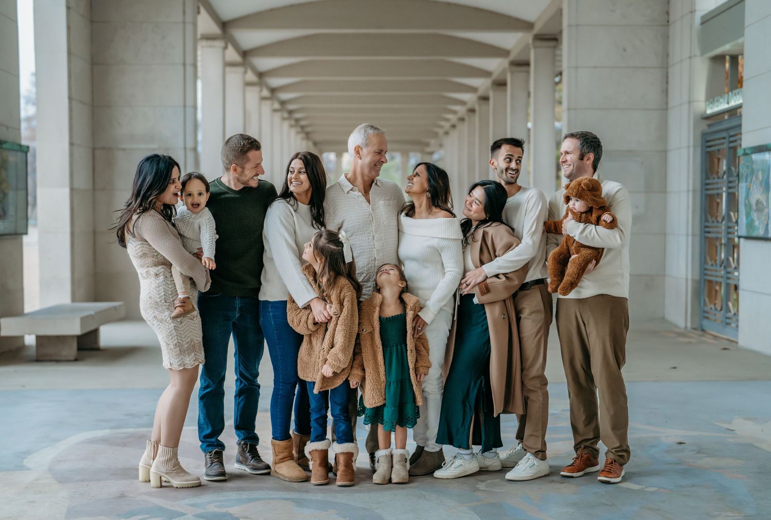 A group of people in coordinating beige and brown outfits stand together in an outdoor covered walkway.