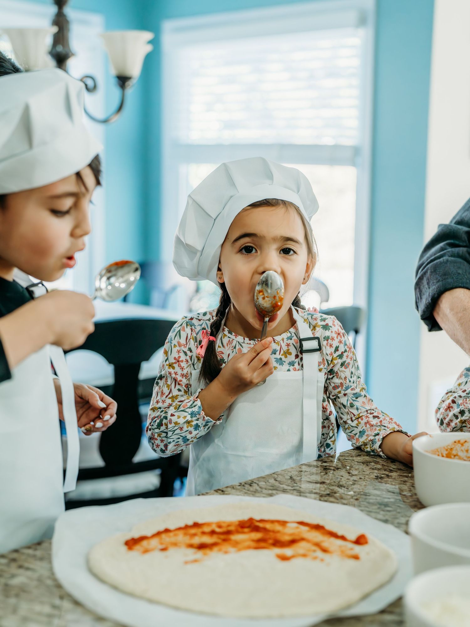 A sequence of photos showing hands spreading sauce ingredients on pizza dough in a bright turquoise kitchen.