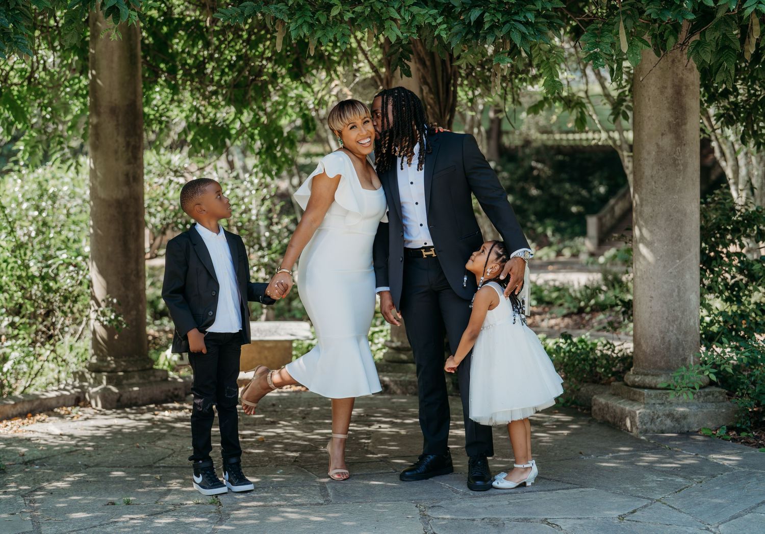 A wedding party joyfully poses for candid photos in a series of shots under shady trees in an outdoor setting.