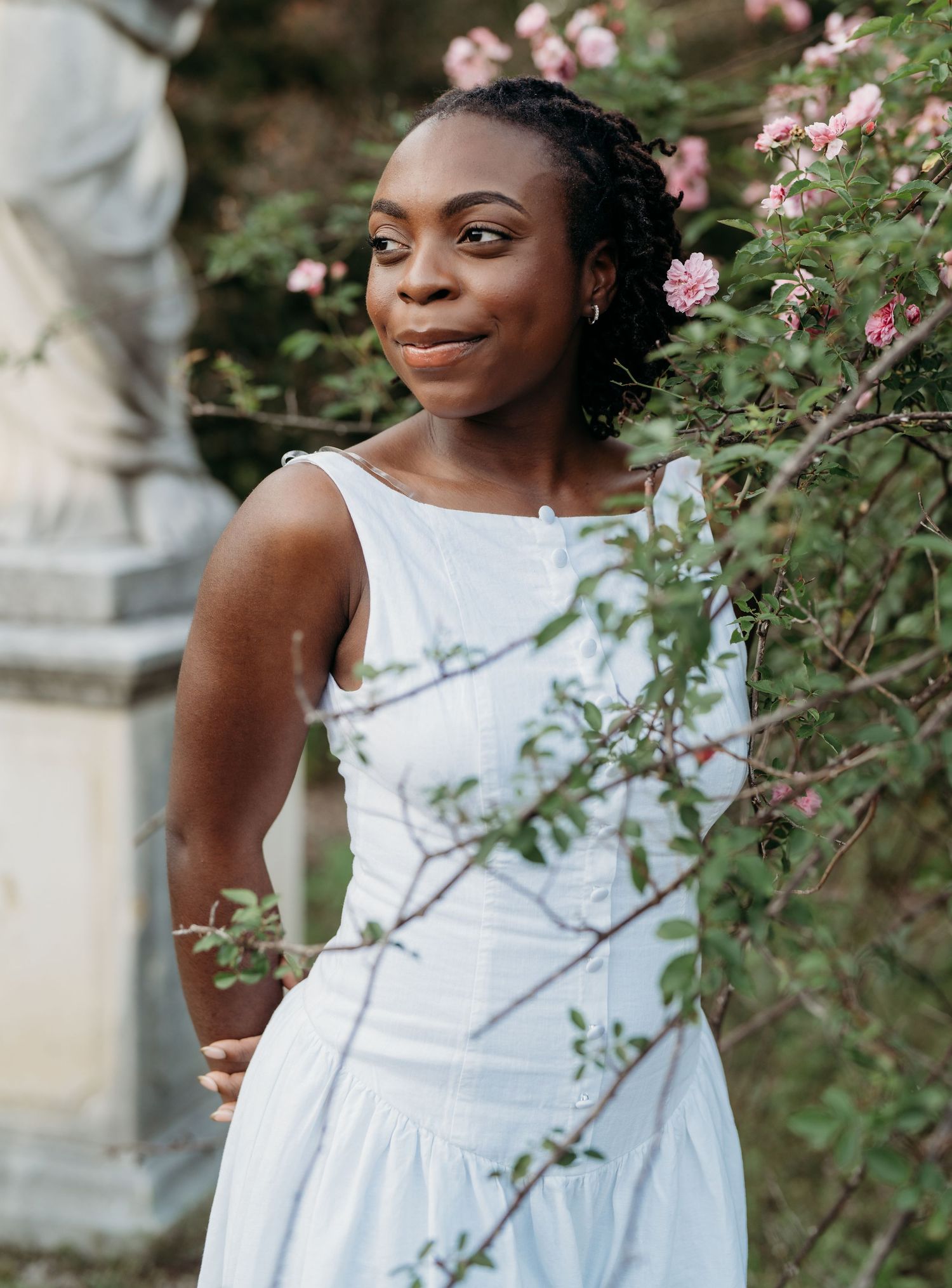 Beautiful wedding photo of a bride in a white dress with braided hair standing among delicate pink roses in a garden setting.