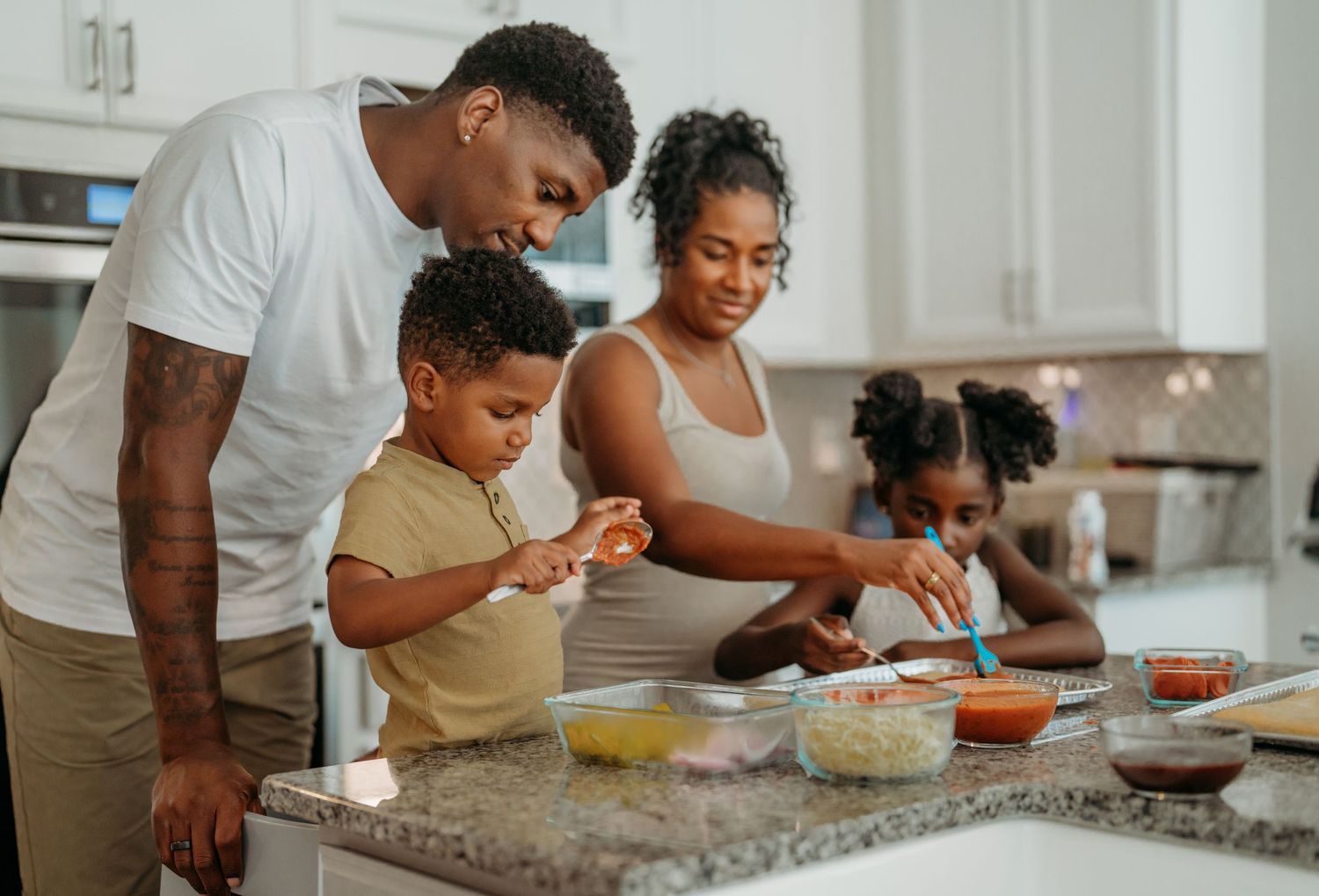 Happy family preparing a meal together in their bright modern kitchen with white cabinets and granite countertops.