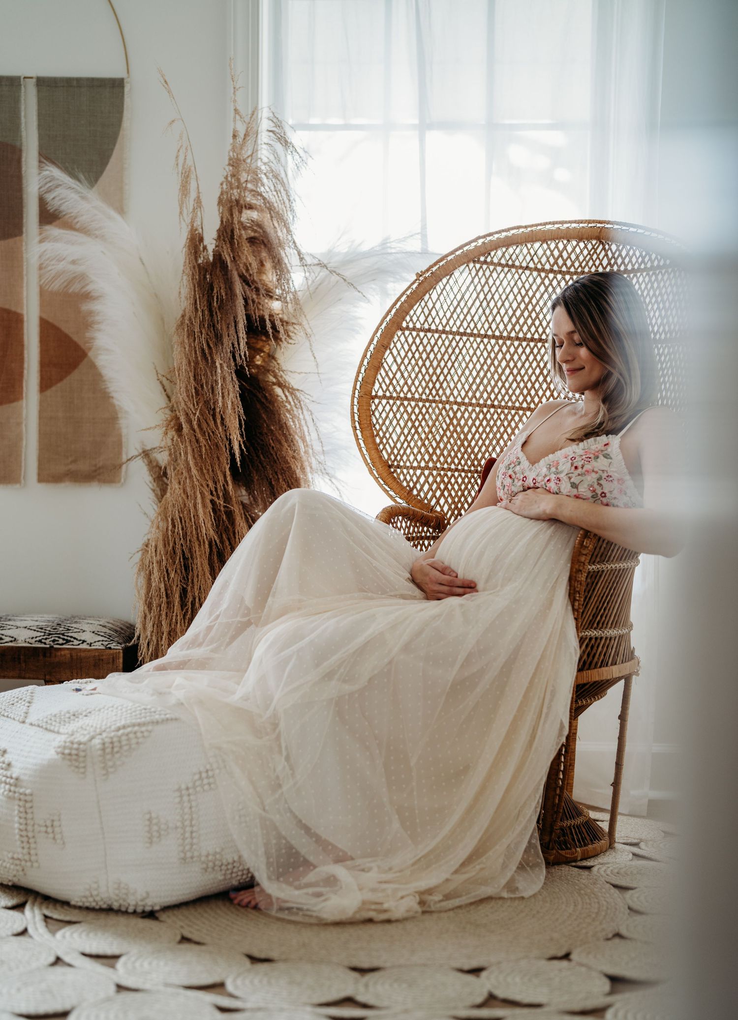 A person in a flowing white dress reclines gracefully on a rattan peacock chair in a bright, minimalist setting.