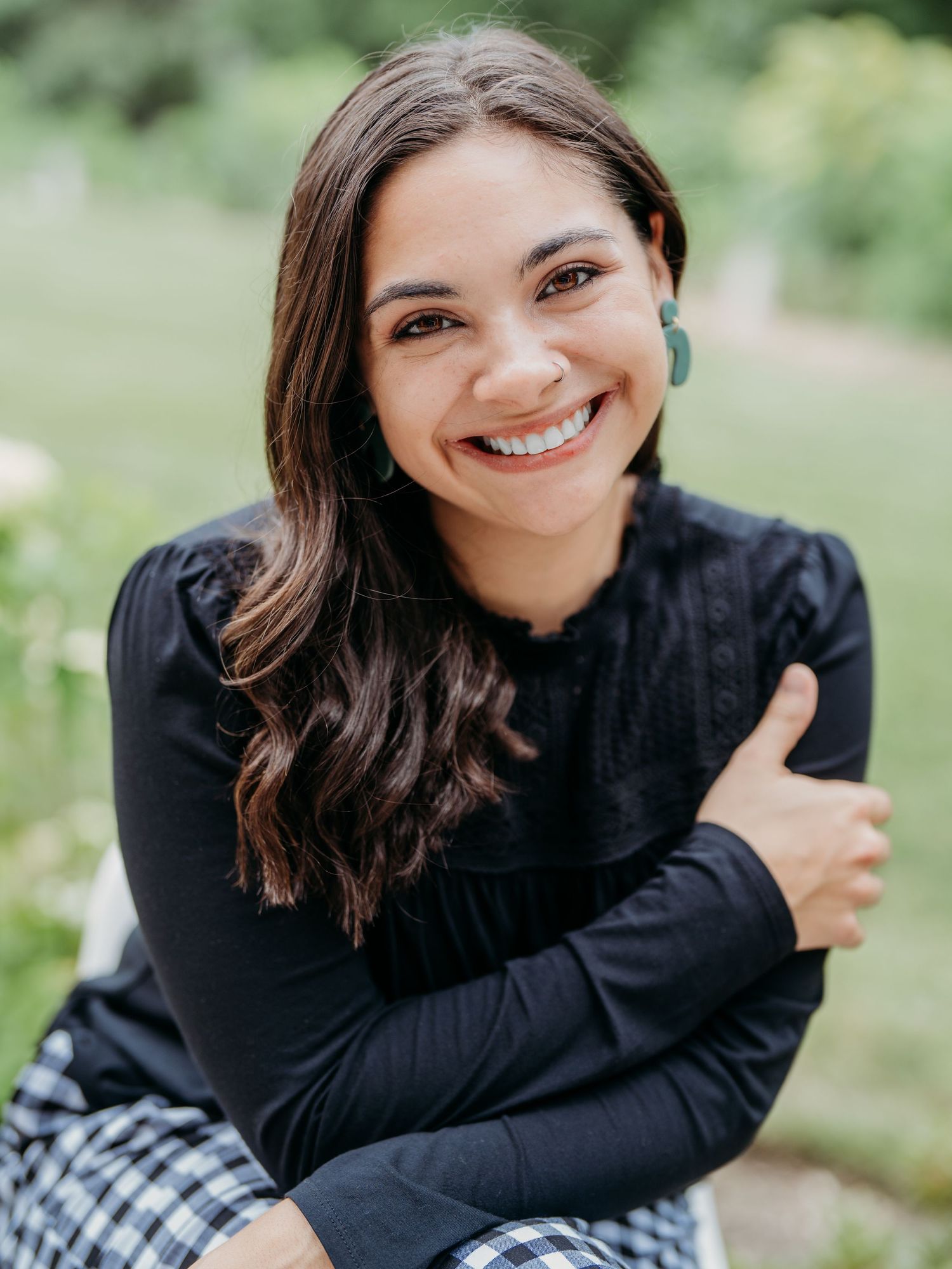 A smiling person in a black sweater poses outdoors with dark hair and a cheerful expression.