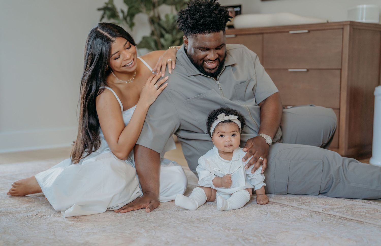 A loving couple relaxes and plays with their baby on a cozy bed with white bedding.