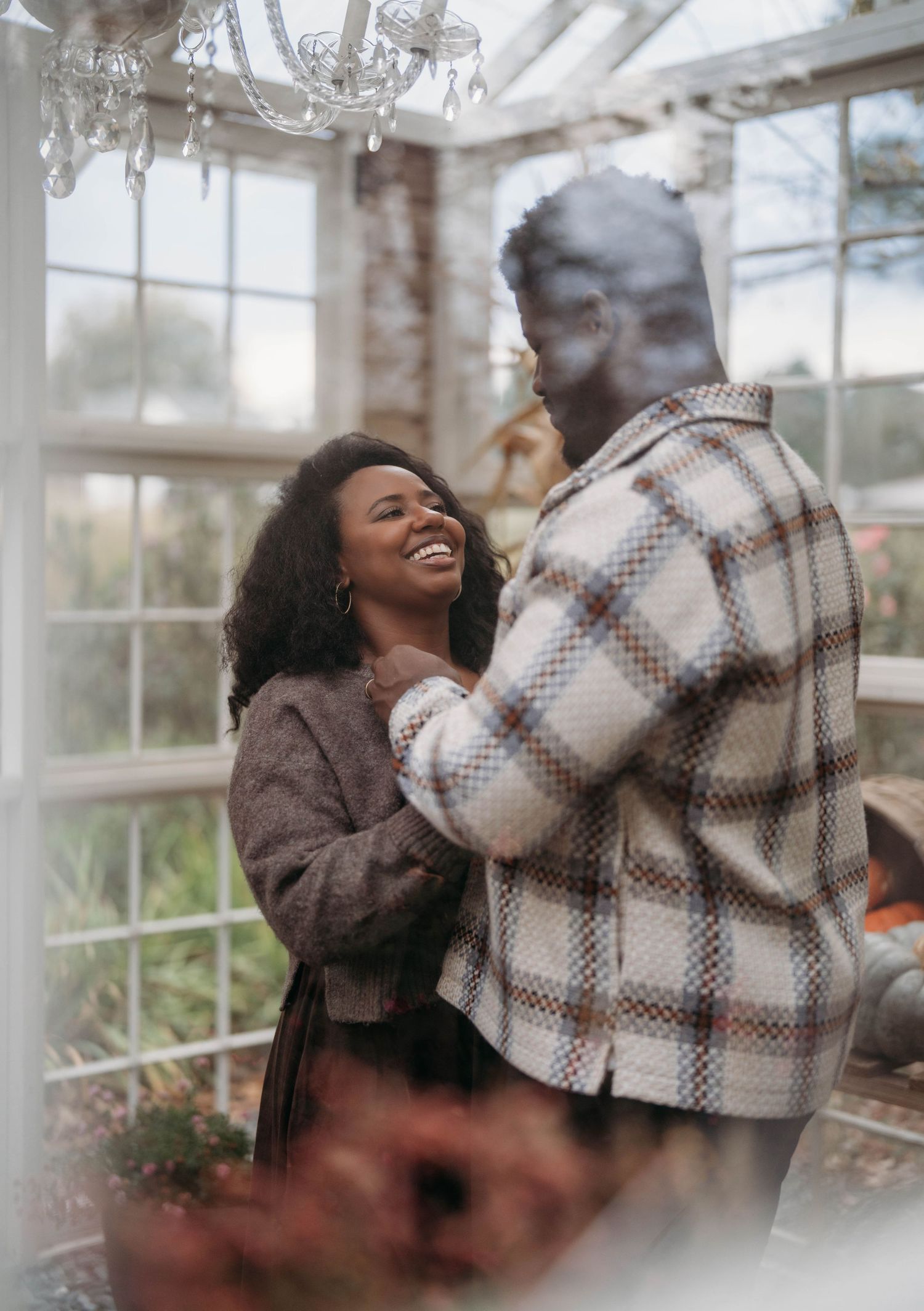 A couple shares a joyful embrace in a bright greenhouse setting with natural light streaming through the windows.