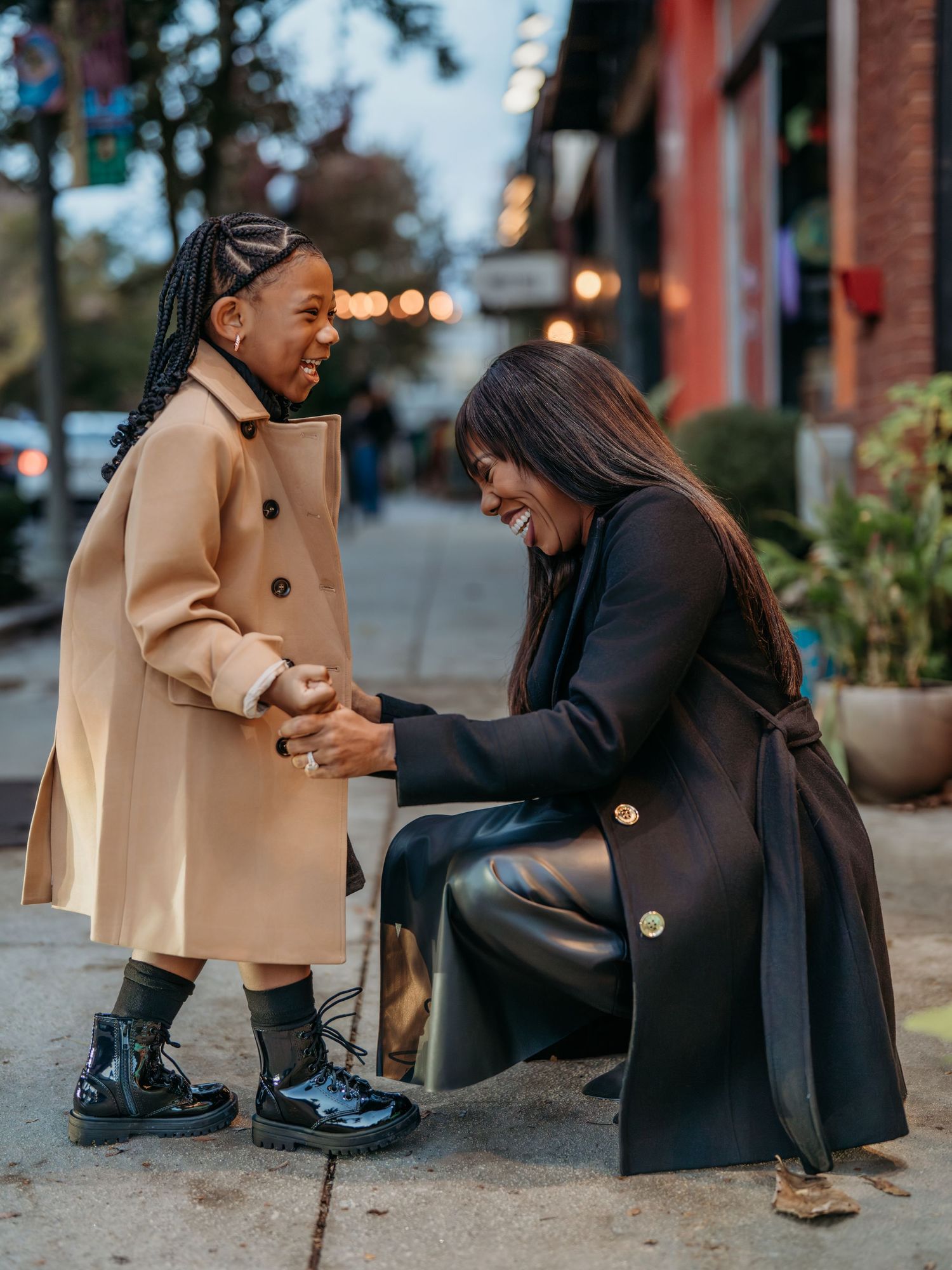 A parent and child in matching tan coats sitting on outdoor steps.