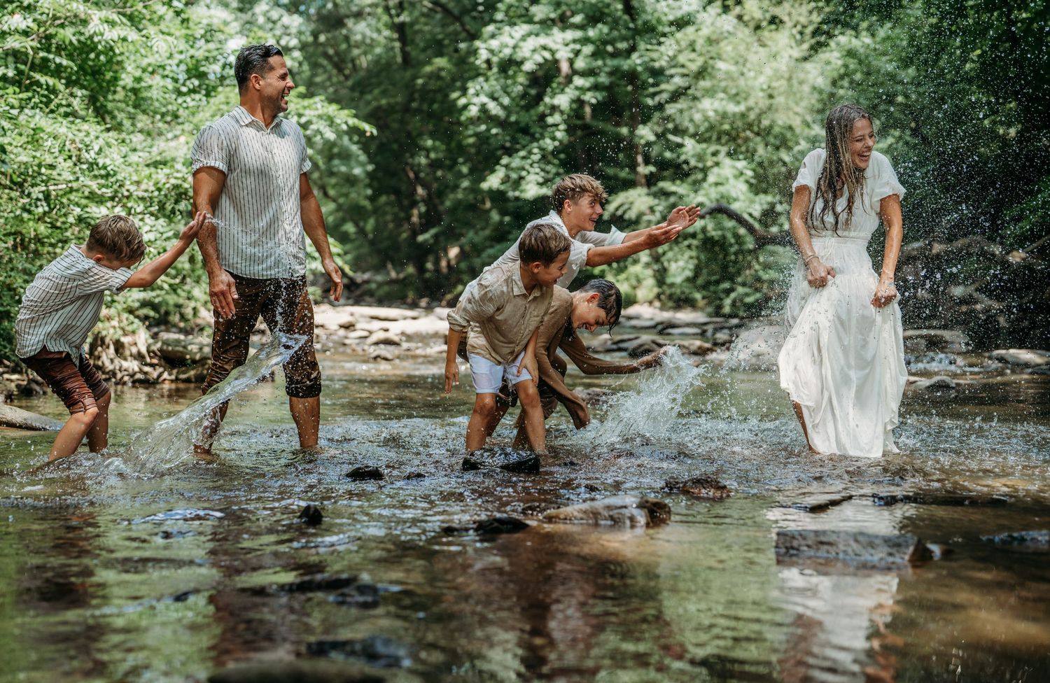 Family enjoys a playful moment splashing and exploring together in a shallow creek surrounded by lush greenery.