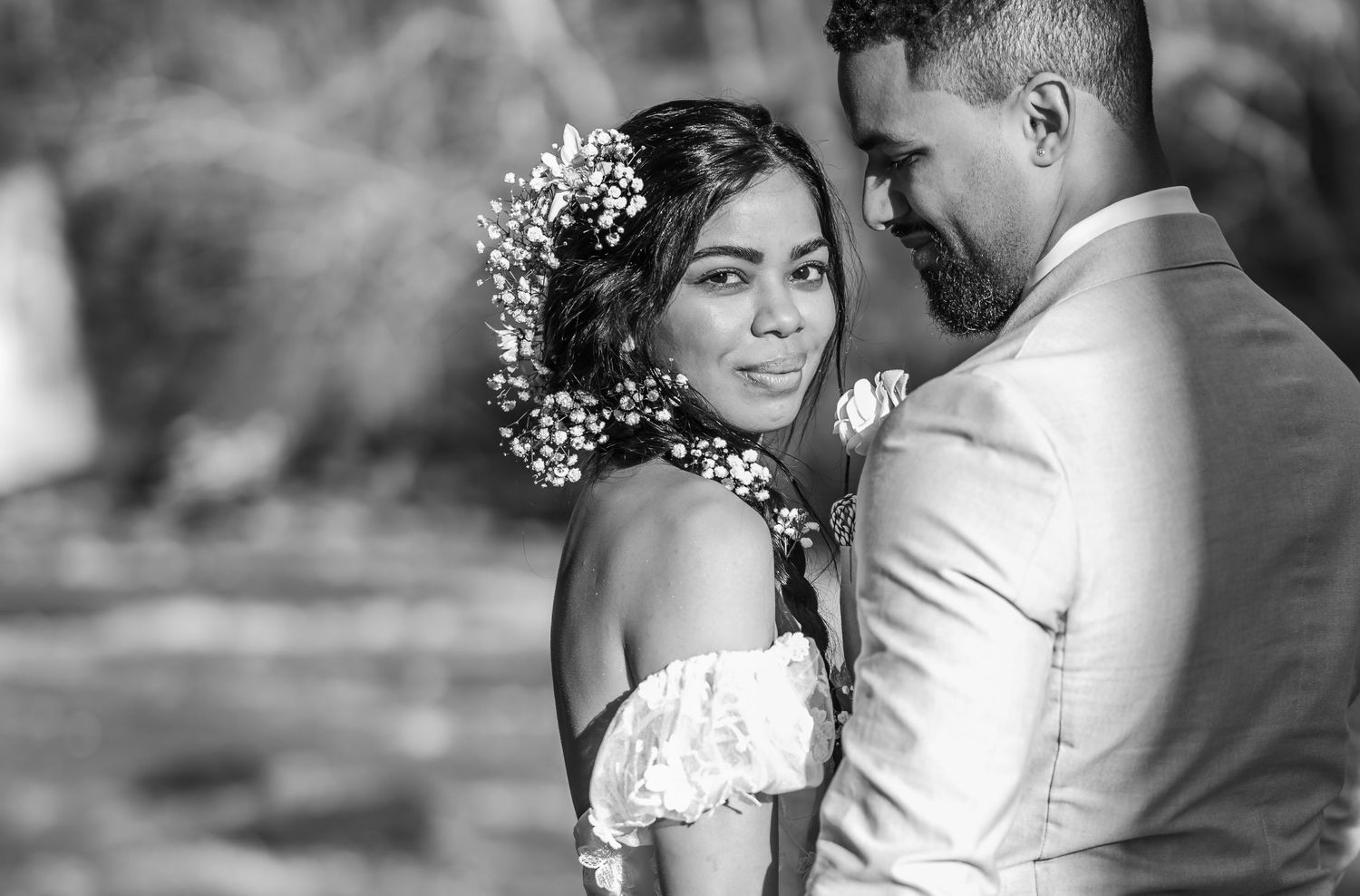 A romantic black and white wedding portrait shows a couple embracing, with the bride wearing a floral crown and off-shoulder dress.