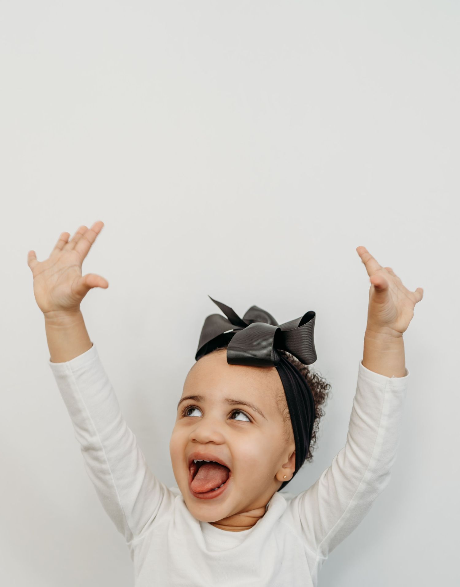 A sequence of four photos showing a baby in white clothing making playful expressions and raising their arms in joy.