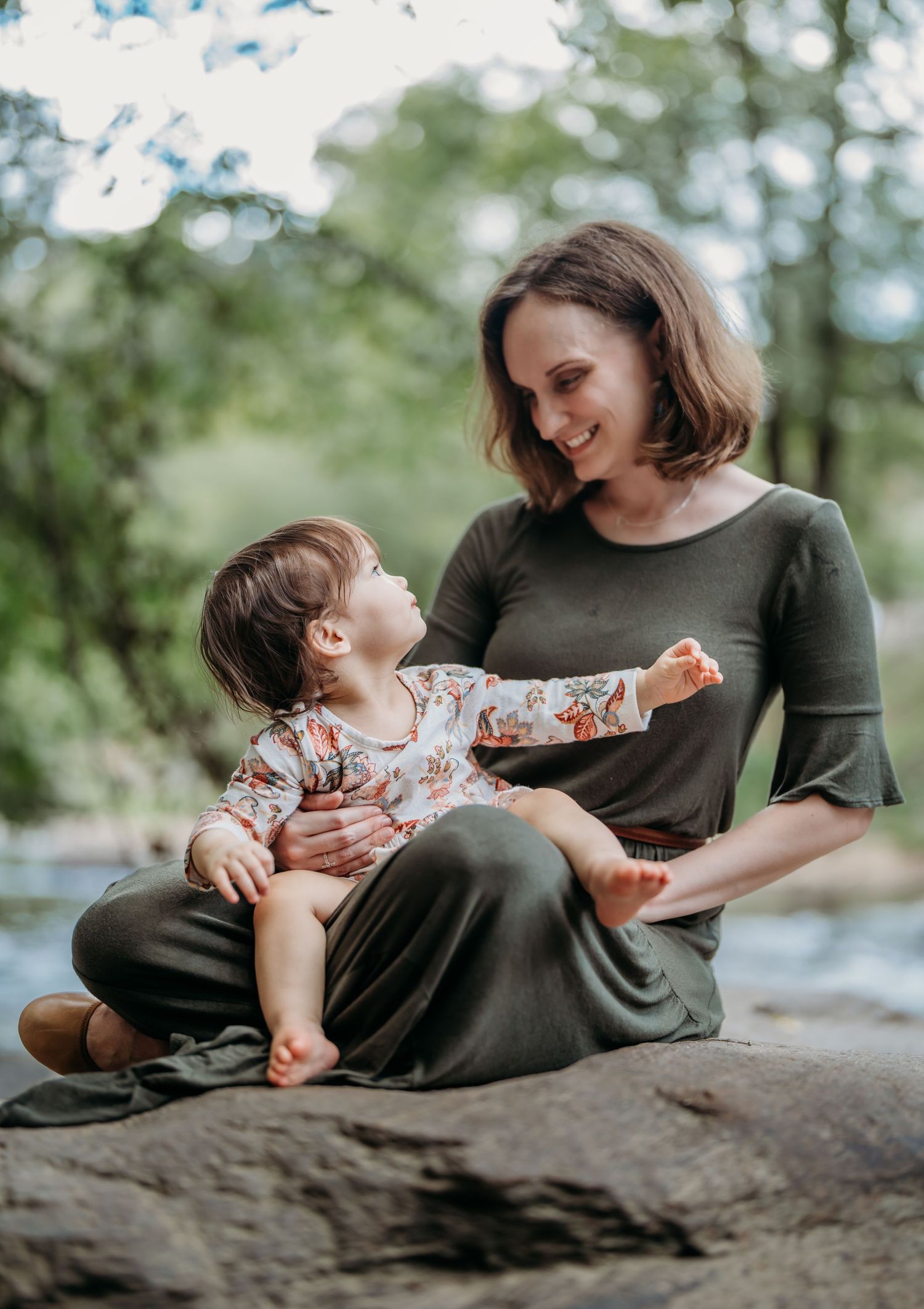 Sweet maternity photography session shows mother and child sharing tender moments on a rock formation in a natural setting.