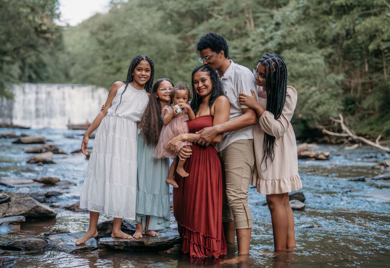 A family wearing coordinated earth-toned outfits poses together near a scenic river during an outdoor photo session.