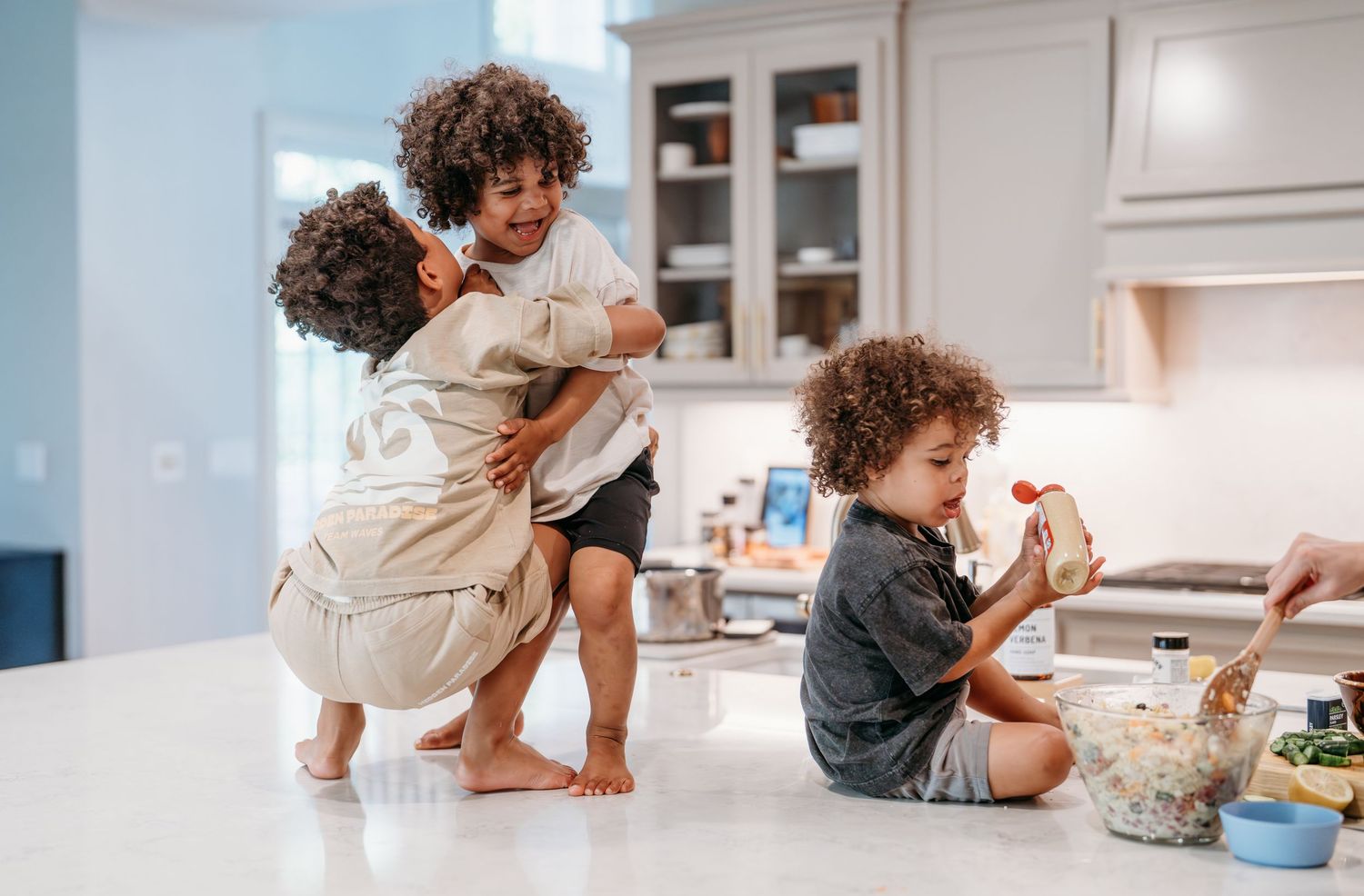 Kids having fun baking and playing in a bright modern kitchen with white countertops and cabinets.
