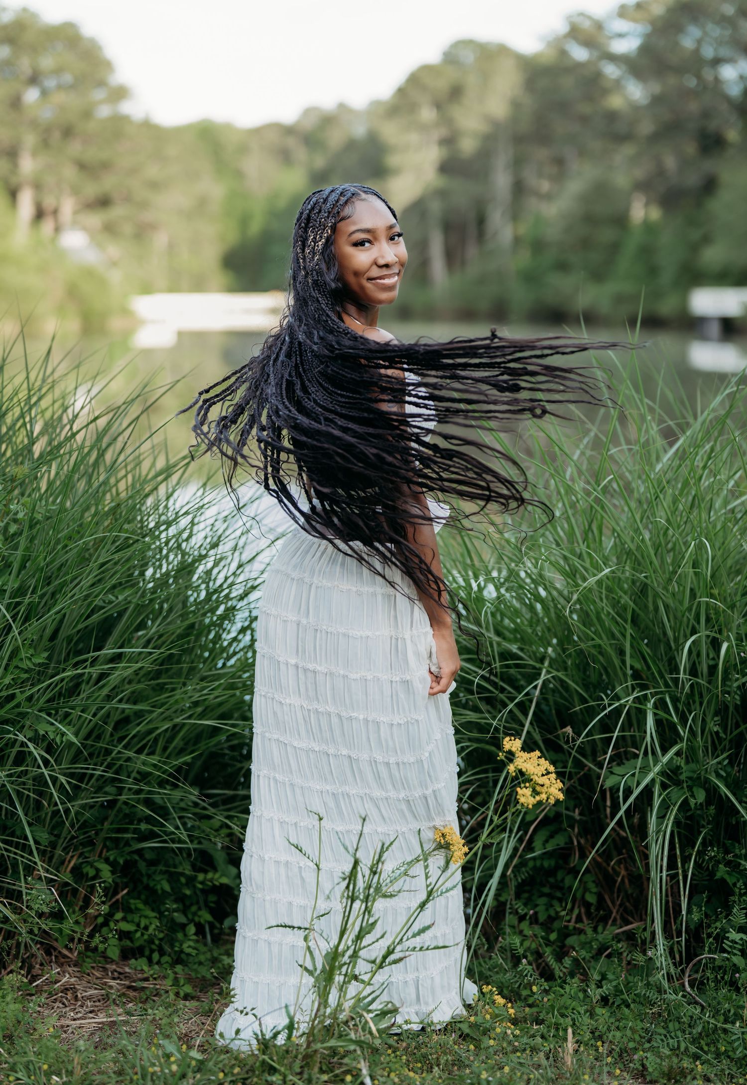Person in a white tiered maxi dress twirling in front of tall grass on a sunny day.
